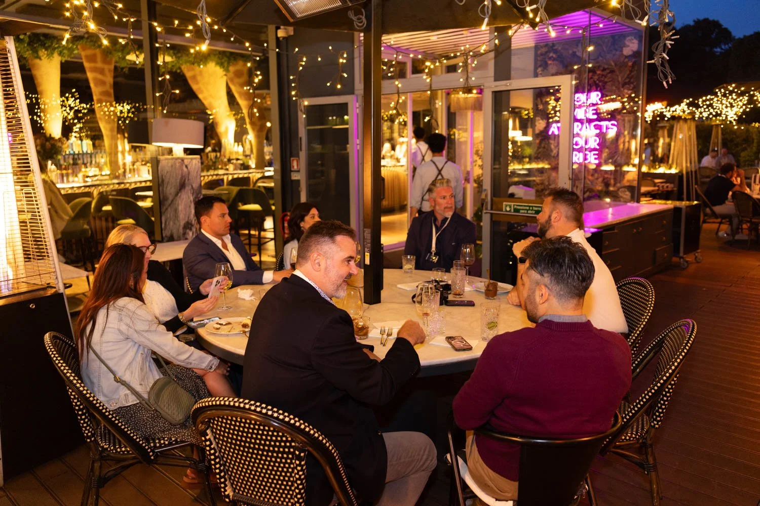 People dining at a round table outside a restaurant during evening, during a corporate event photography session.