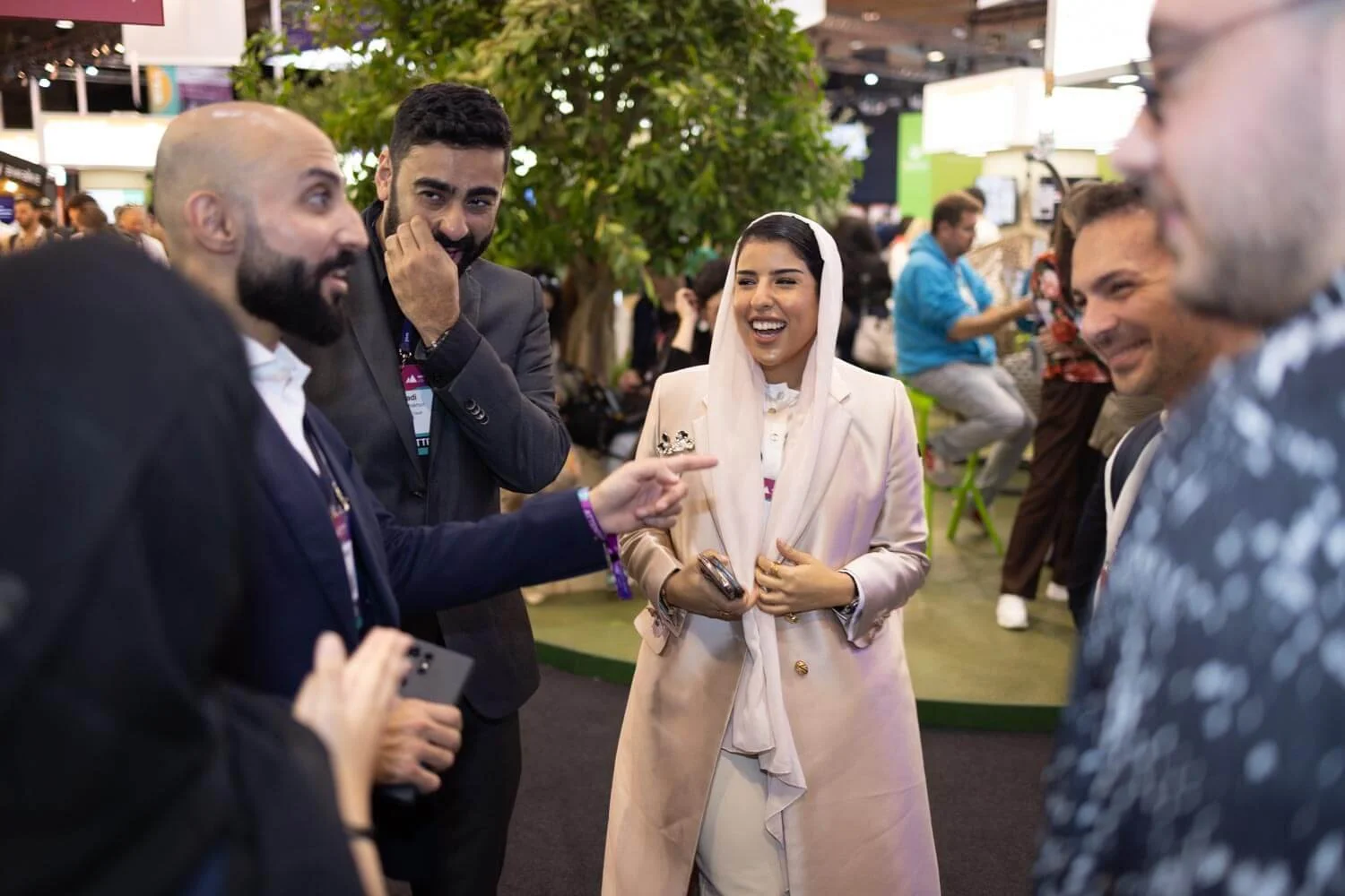 Group of people engaging in conversation at a conference or exhibition, with a woman in a light-colored coat smiling at the center.