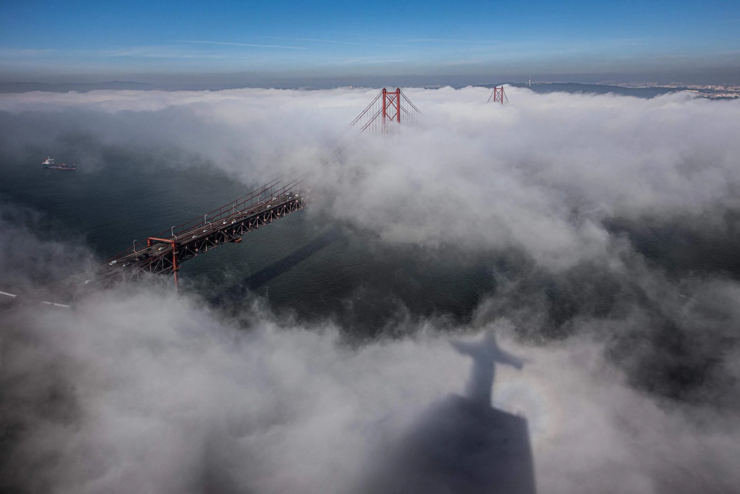 Aerial view of the Golden Gate Bridge partially covered in fog with only the top towers and a section of the roadway visible, and boats in the water below.