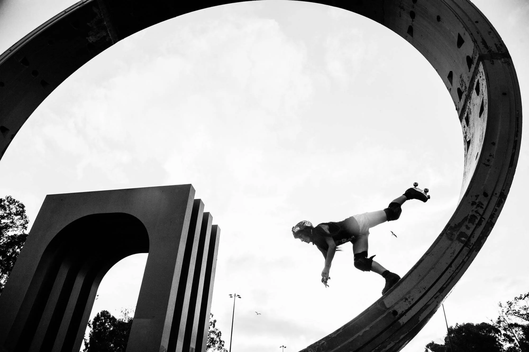 A skateboarder inside a large circular structure, captured in black and white, mid-trick on a skateboarding ramp.