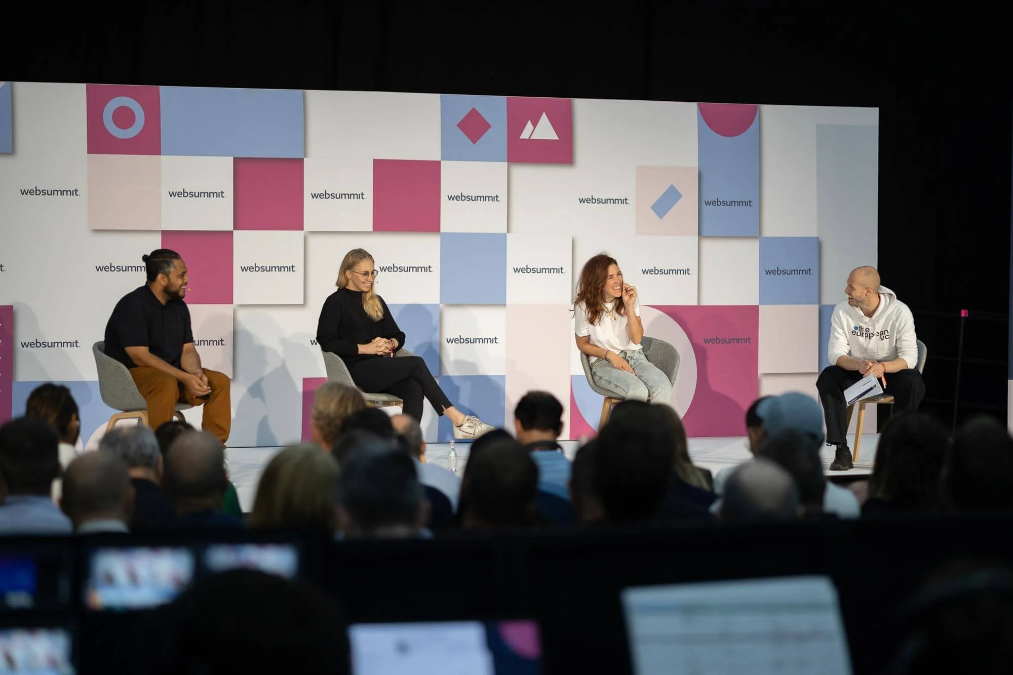 Four people on stage participating in panel discussion at Web Summit, with an audience watching them.