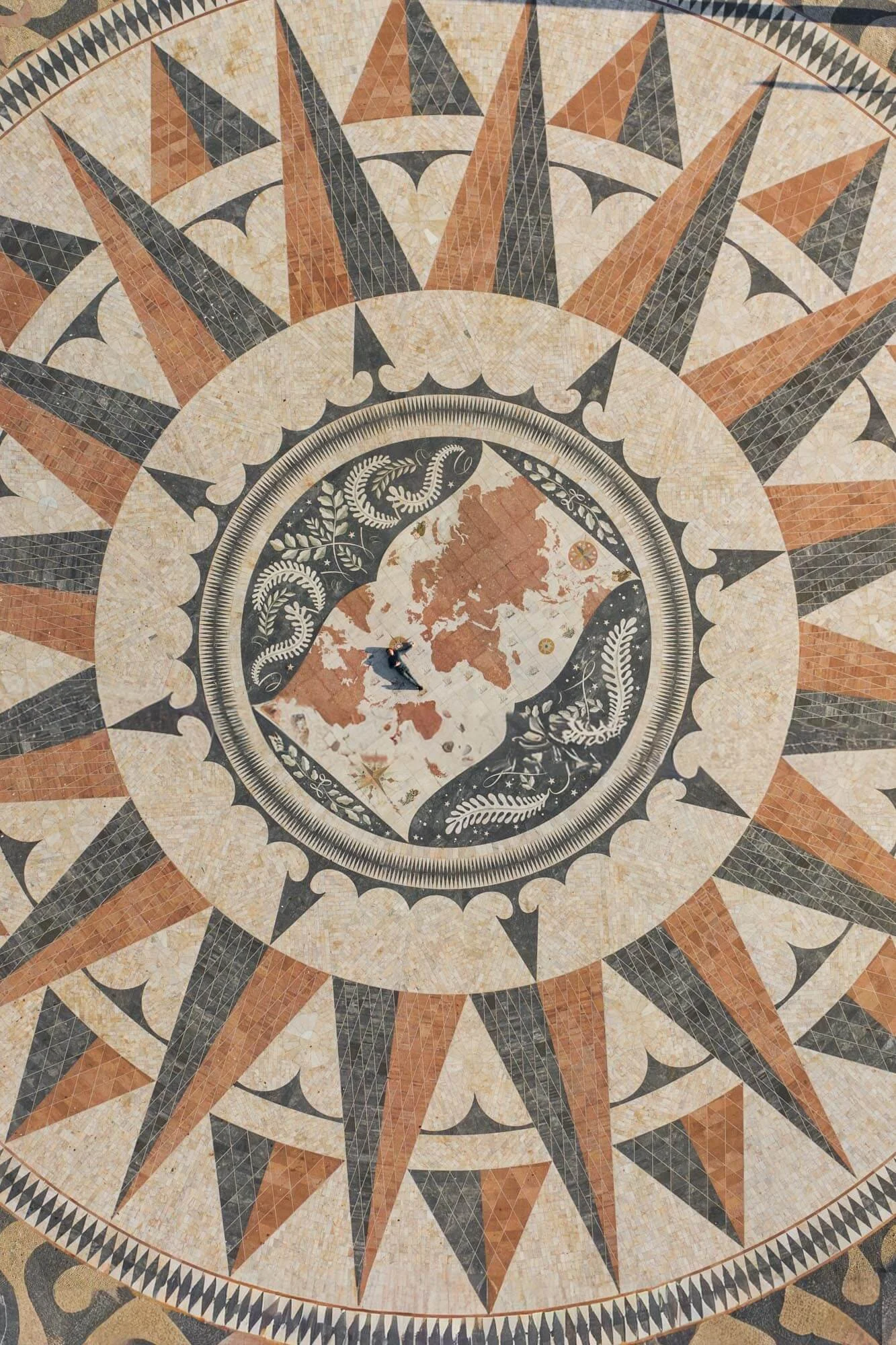 A person walking on a large decorative mosaic floor with a central map of Europe surrounded by a compass design, featuring earthy colors like beige, brown, and black.