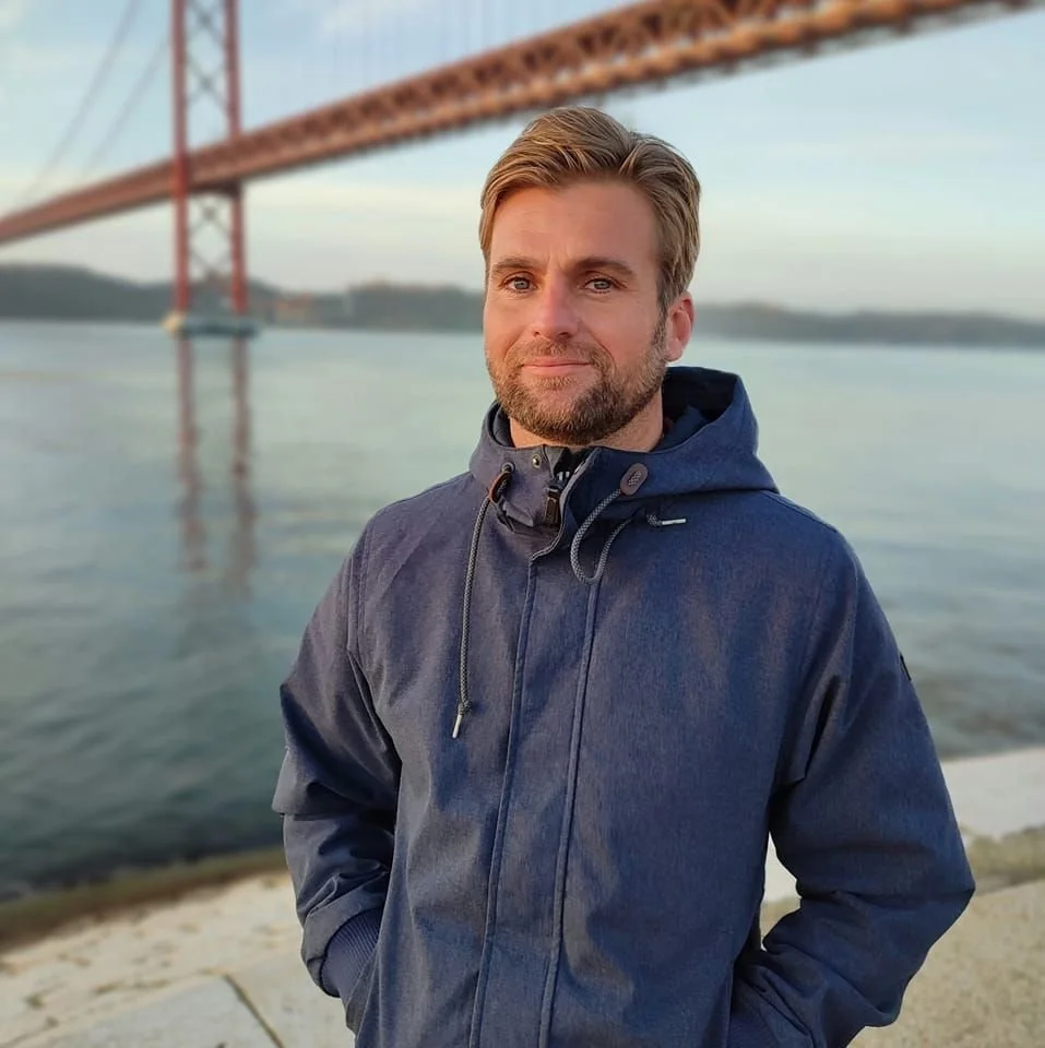 A portrait of a Lisbon Photographer,  near the water with a bridge in the background.