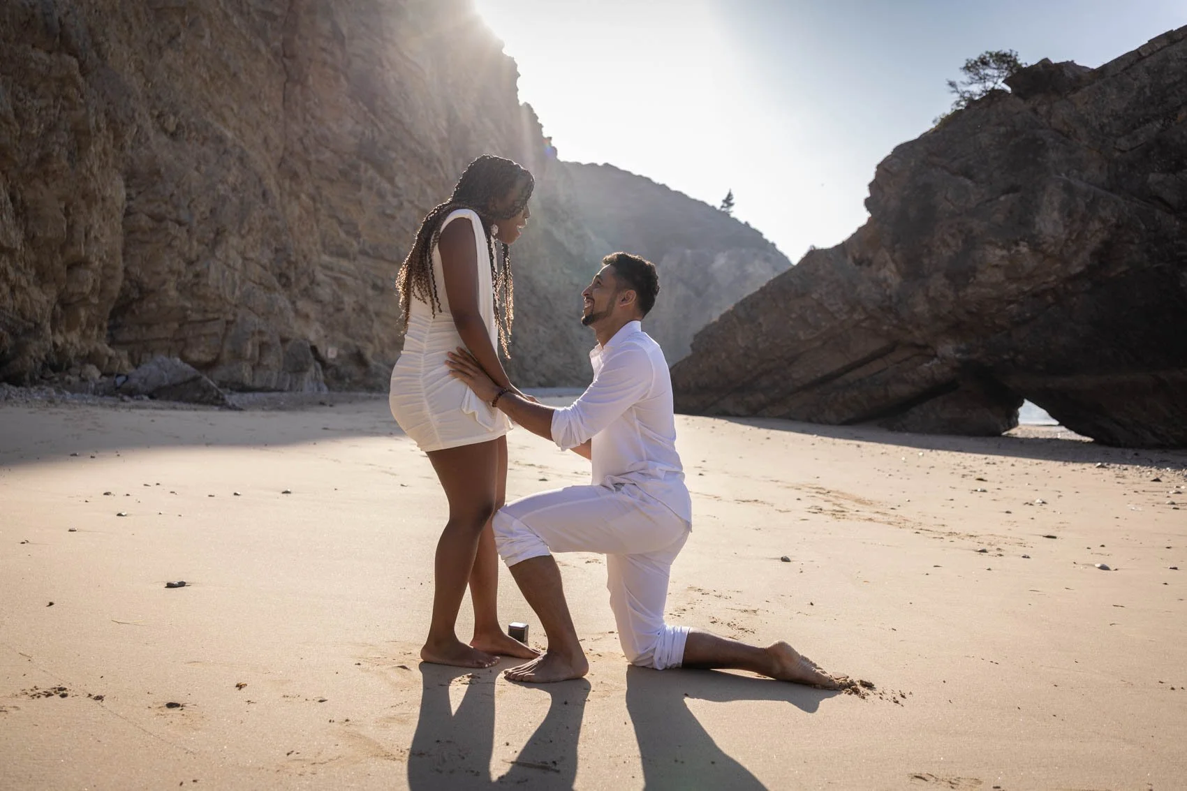 Man and woman dressed in white at secluded beach. Mad proposing a woman on the knees. Surprise proposal at Ribeira de Cavalo beach.