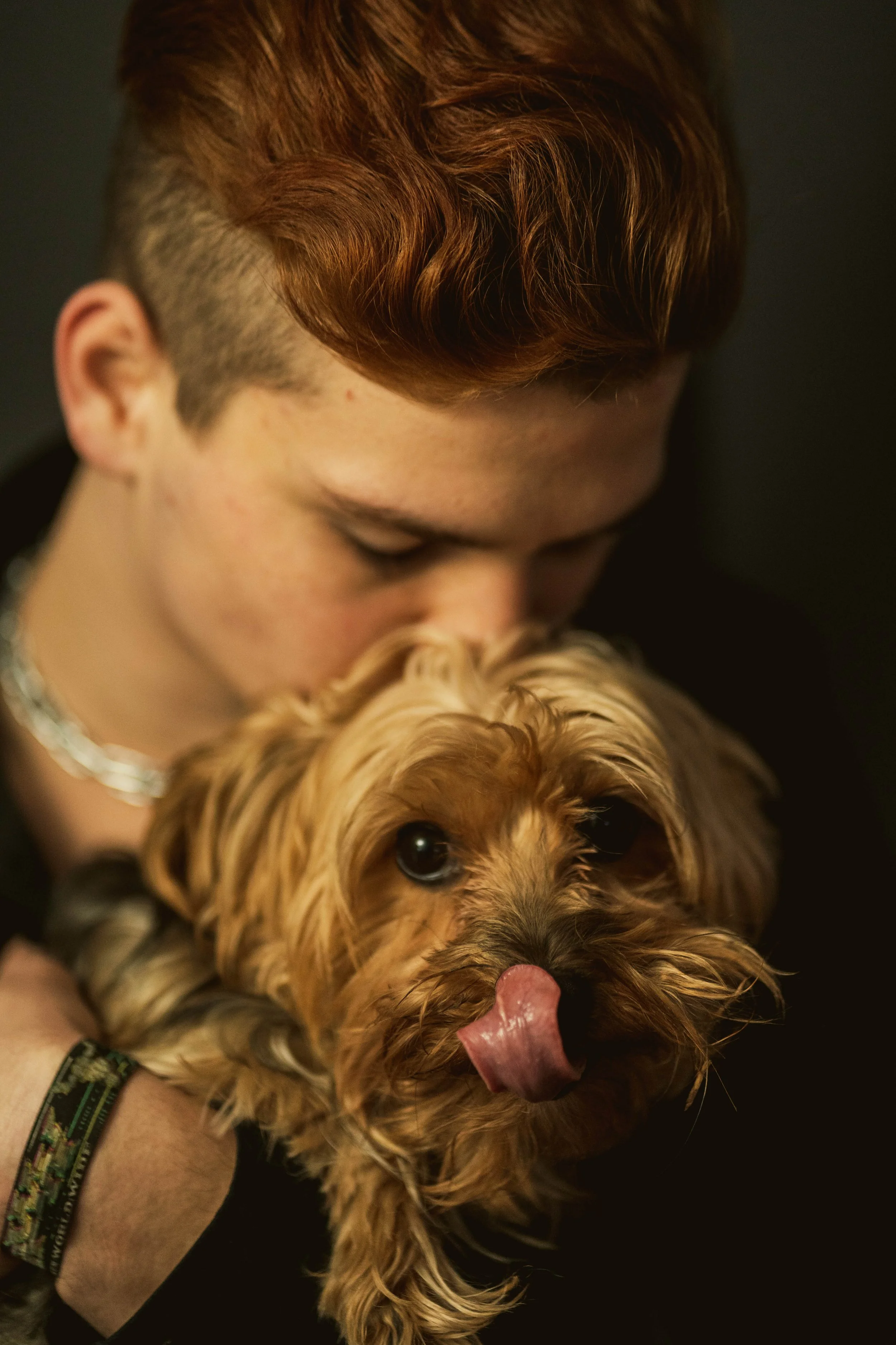 Junge Person mit roten Haaren hält einen kleinen Hund, der gerade seinen Zungenfinger leckt.