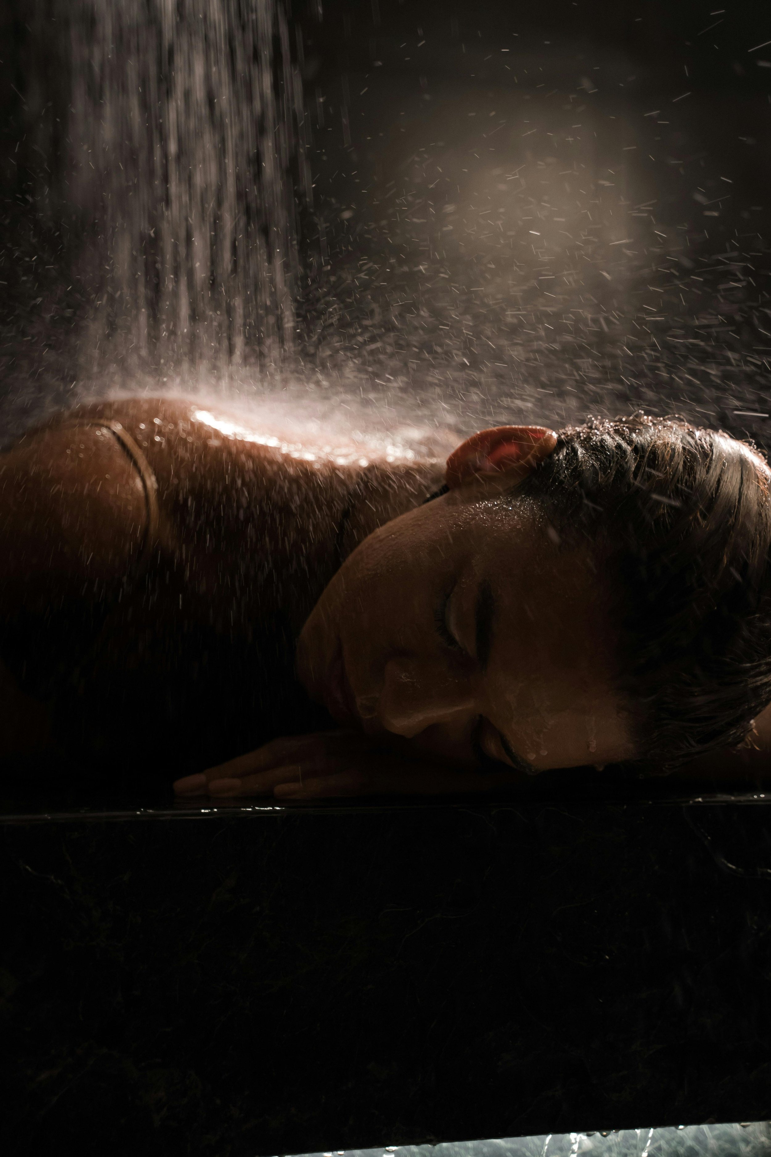 Une personne faisant une séance de massage ou de spa, allongée sur le côté, sous une douche ou une pluie fine avec de la vapeur et des gouttes d'eau