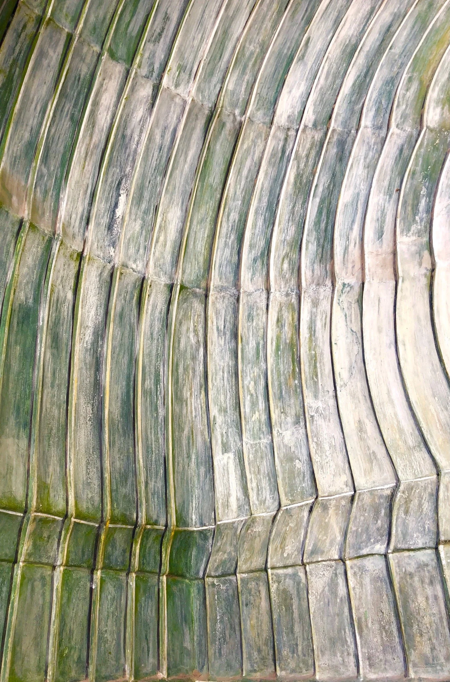 Close-up of curved, weathered greenish-gray roof tiles arranged in a wavy pattern.