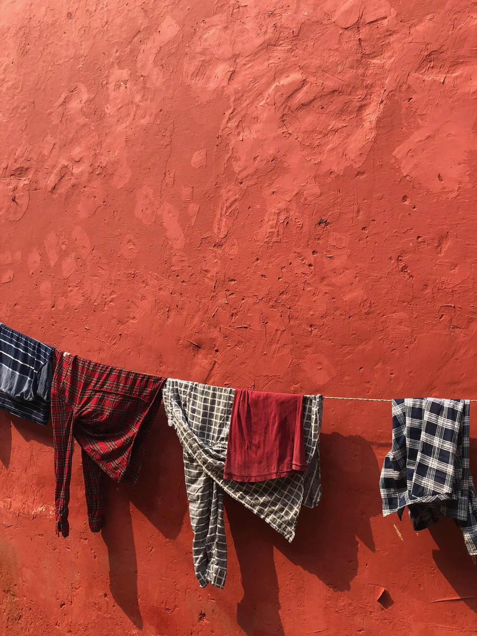 Clothes hanging on a clothesline against a reddish, textured wall.