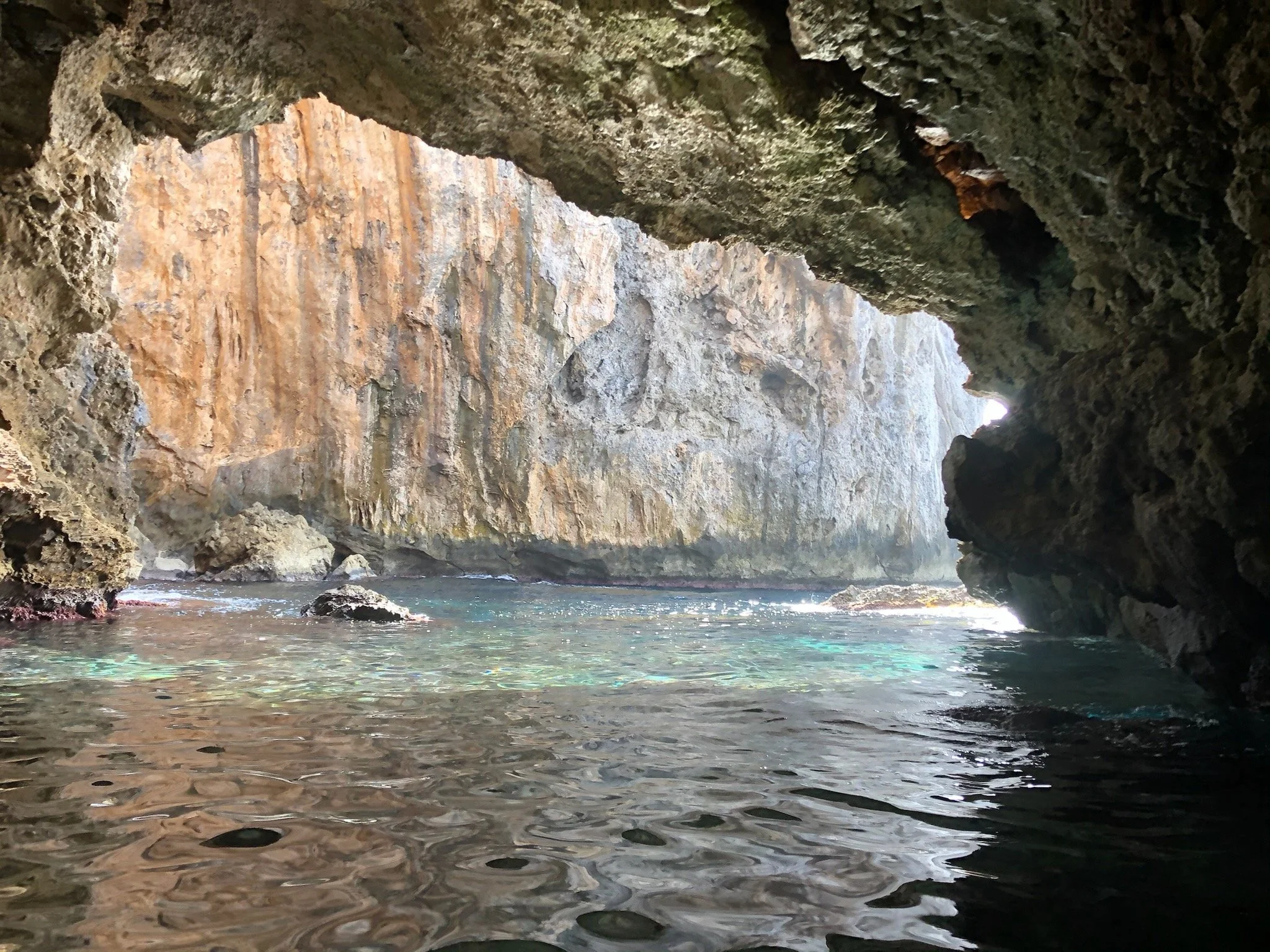 Seascape viewed from inside a rocky cave with water and a large cliff in the background.