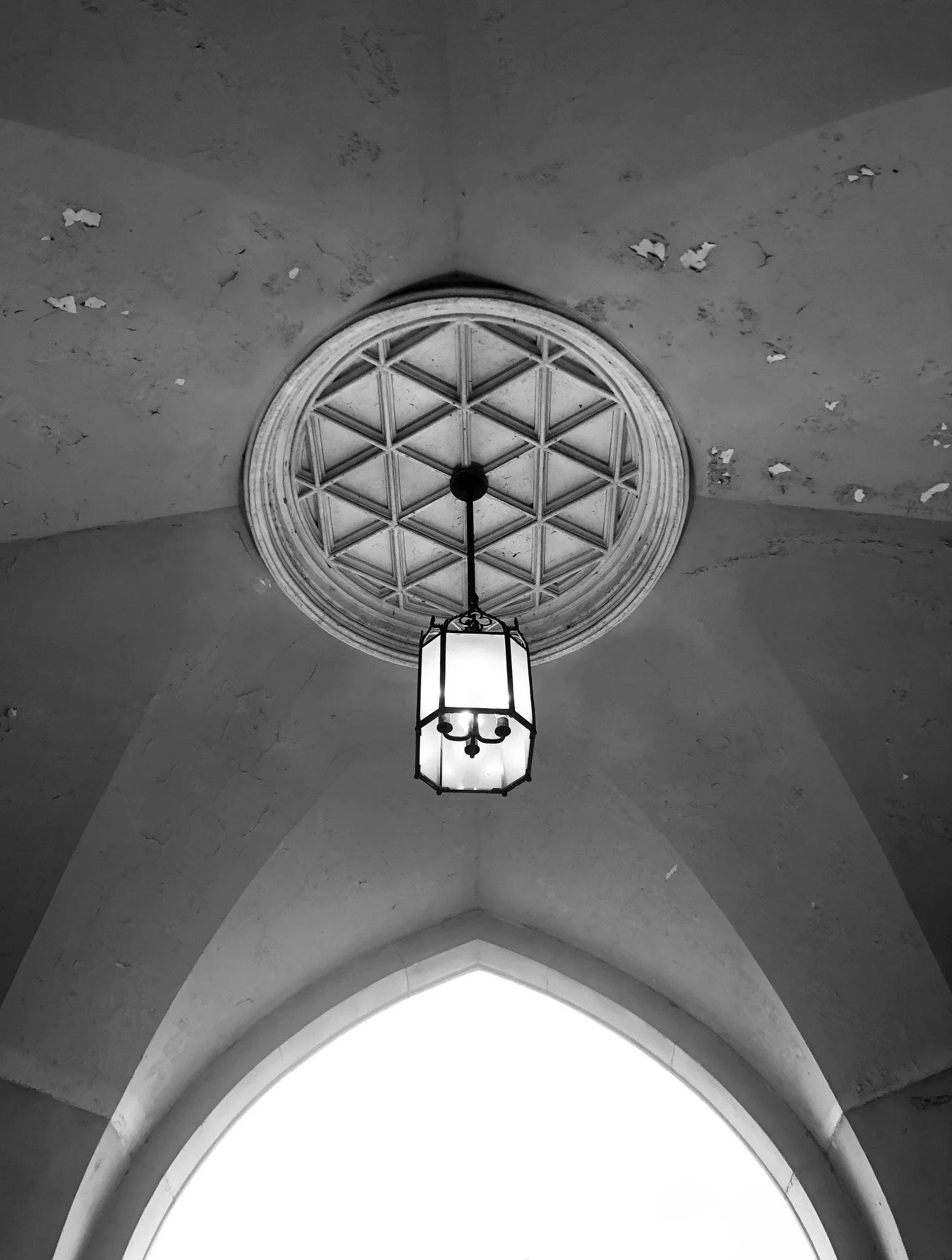 Black and white photo of an ornate ceiling with a hanging lantern and a circular decorative window with a geometric pattern.