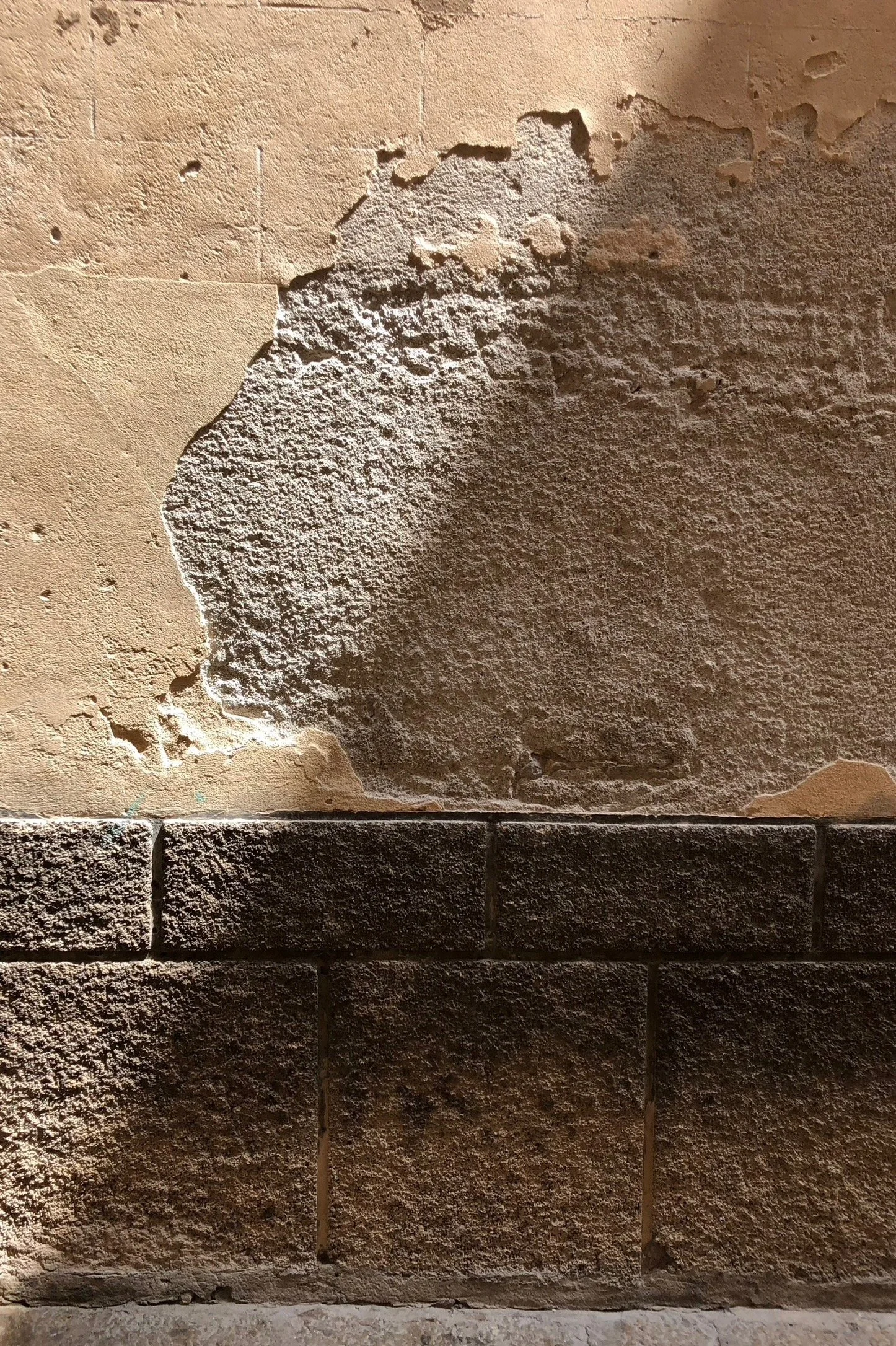 Close-up of a wall showing damaged and weathered paint and brickwork, with a large section of plaster peeling away.
