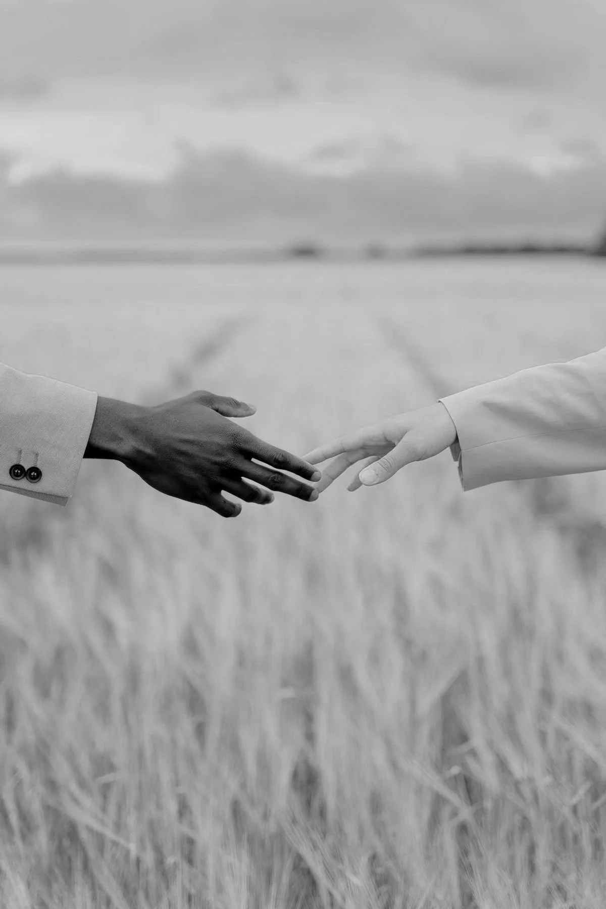 Two people reaching out to hold hands in a field, black and white photo.