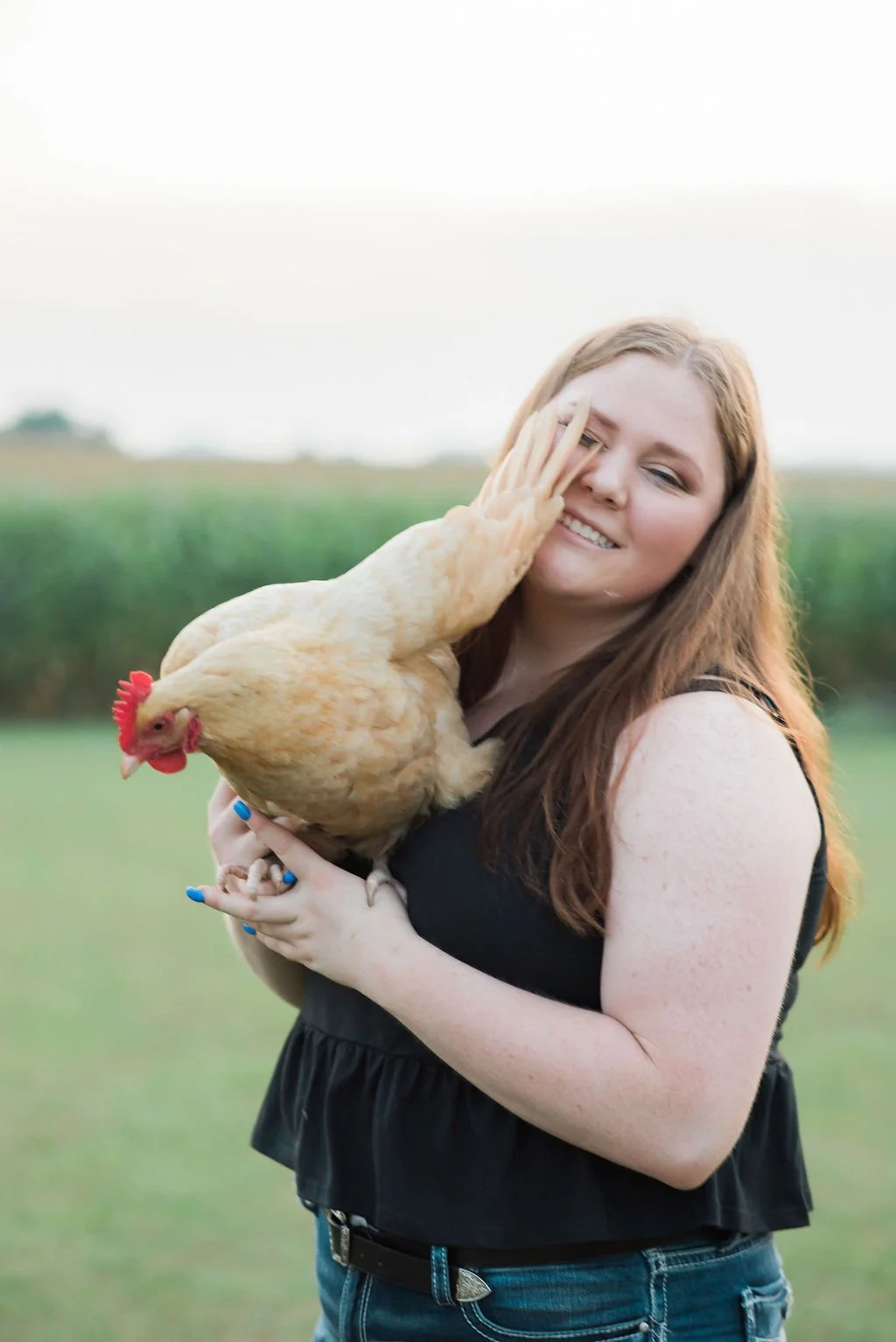 A woman with red hair holding a chicken outdoors in a field.