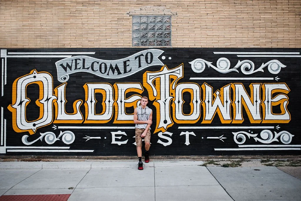 A person standing in front of a mural that says "Welcome to Olde Towne East" painted on a brick wall.