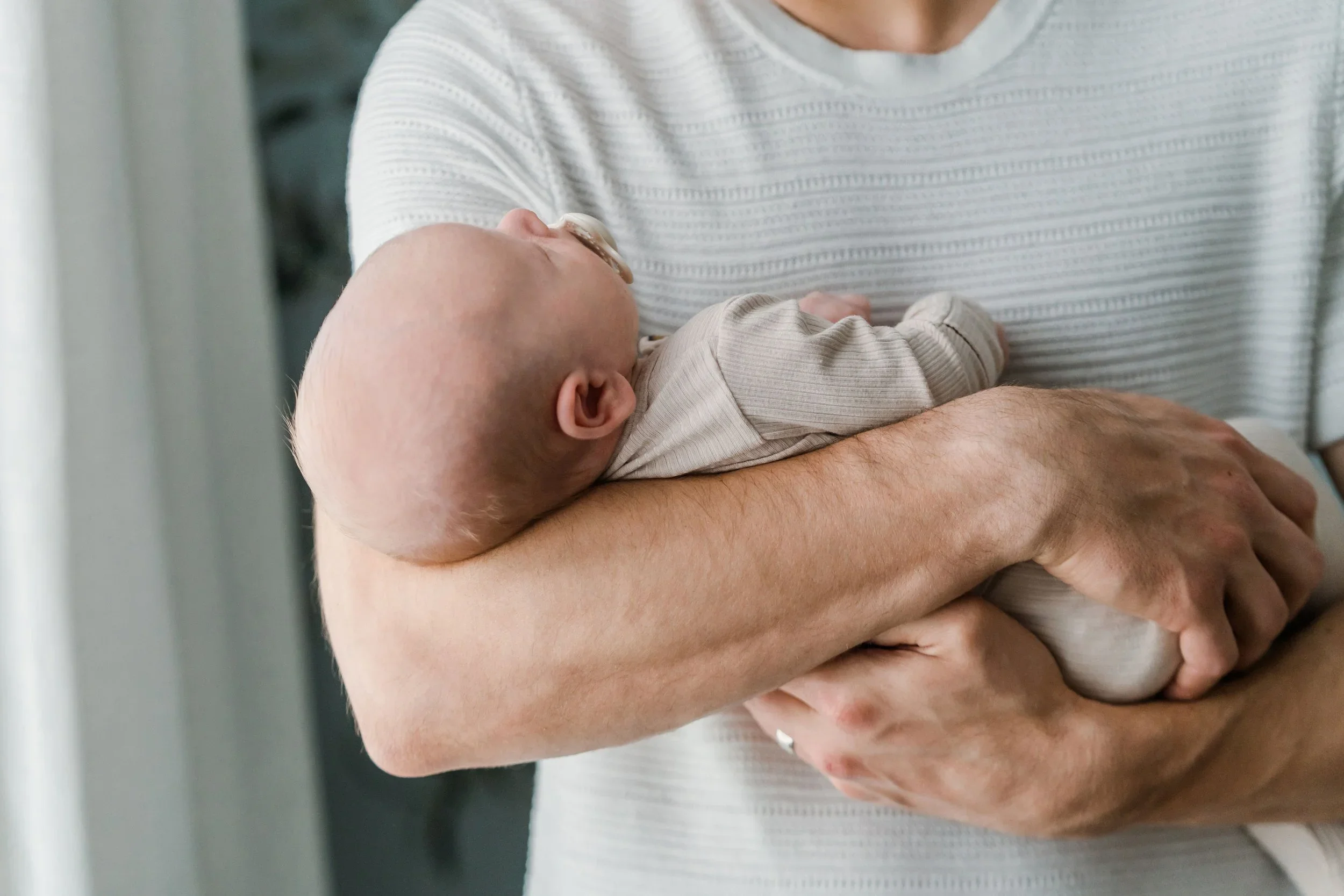 A close-up of a baby held in an adult's arm, with the baby's head resting on the adult's chest