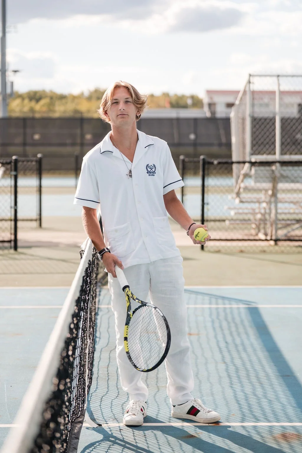Young person standing on outdoor tennis court holding tennis racket and tennis ball.