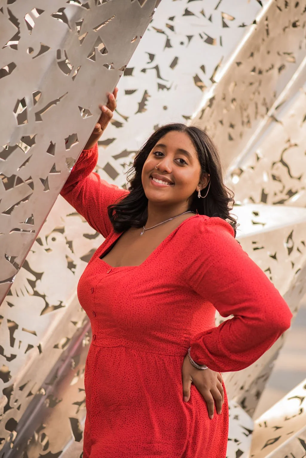 A woman in a red dress smiling, standing amidst large white decorative panels with intricate cut-out patterns.