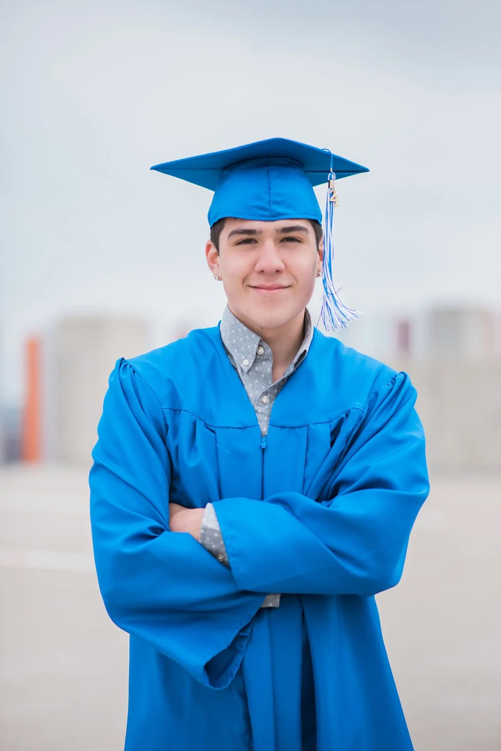 A young man in a graduation cap and gown standing outdoors with buildings in the background