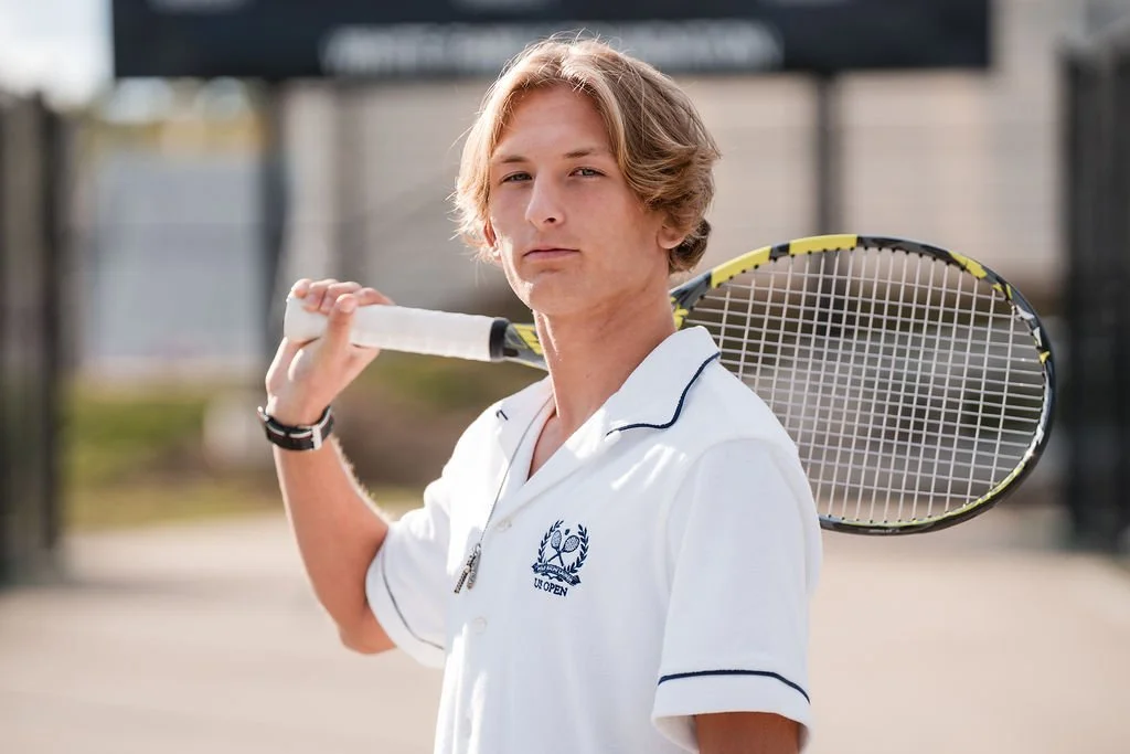 Young man with blonde hair holding a tennis racket over his shoulder on a tennis court.
