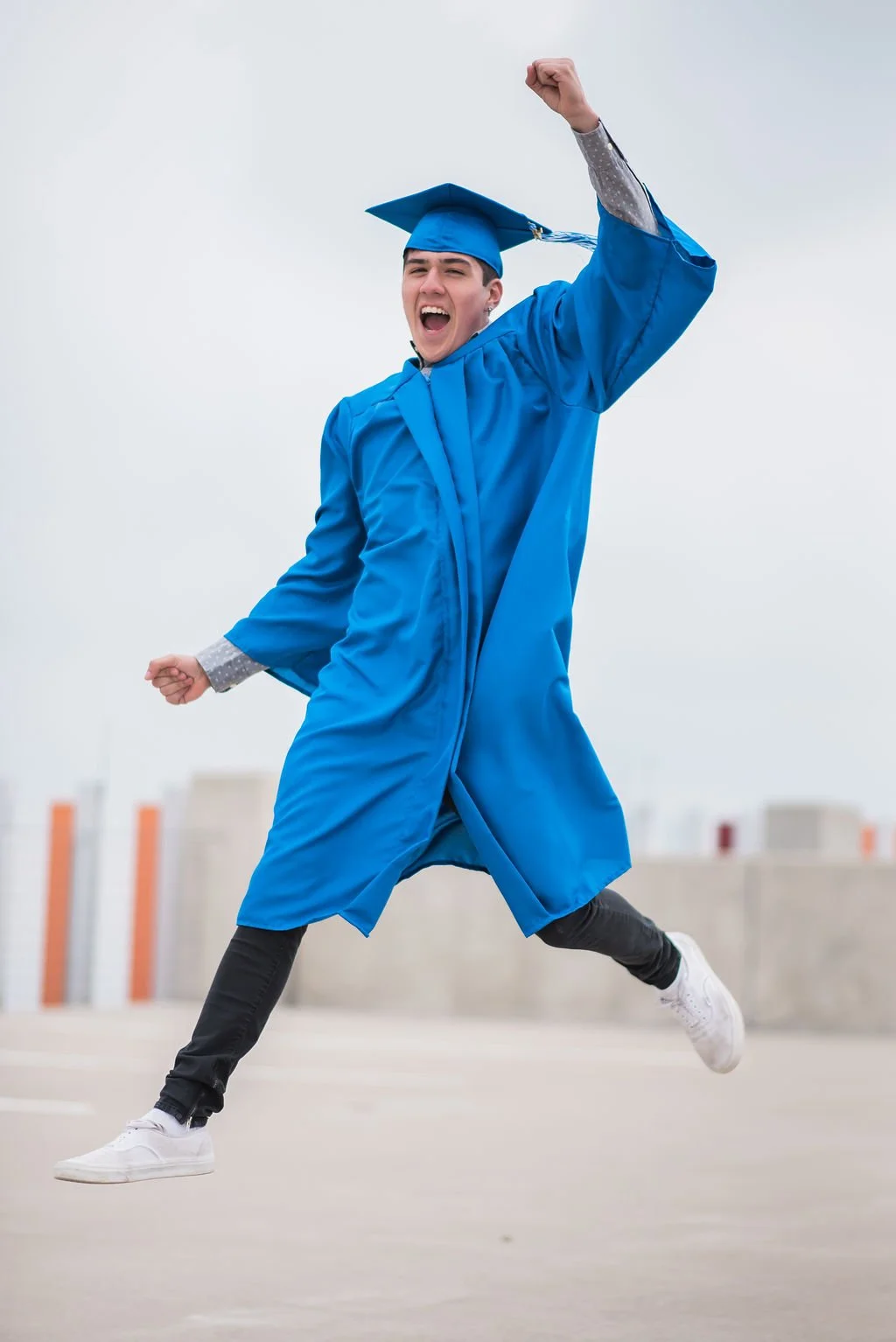 Young man in blue graduation gown and cap celebrating outdoors.