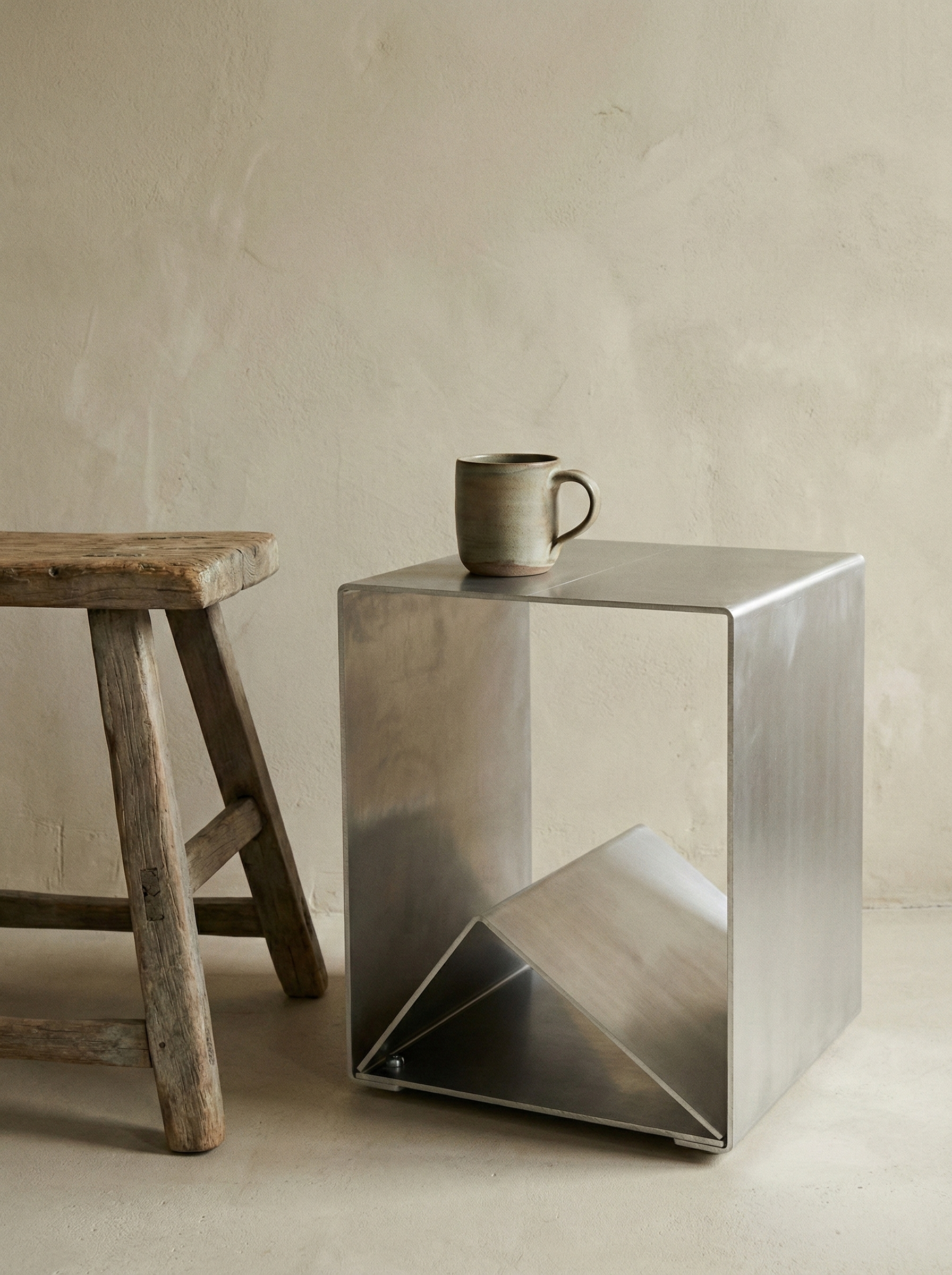 A rustic wooden bench and a modern metal box with a ceramic mug on top, set against a plain beige wall.