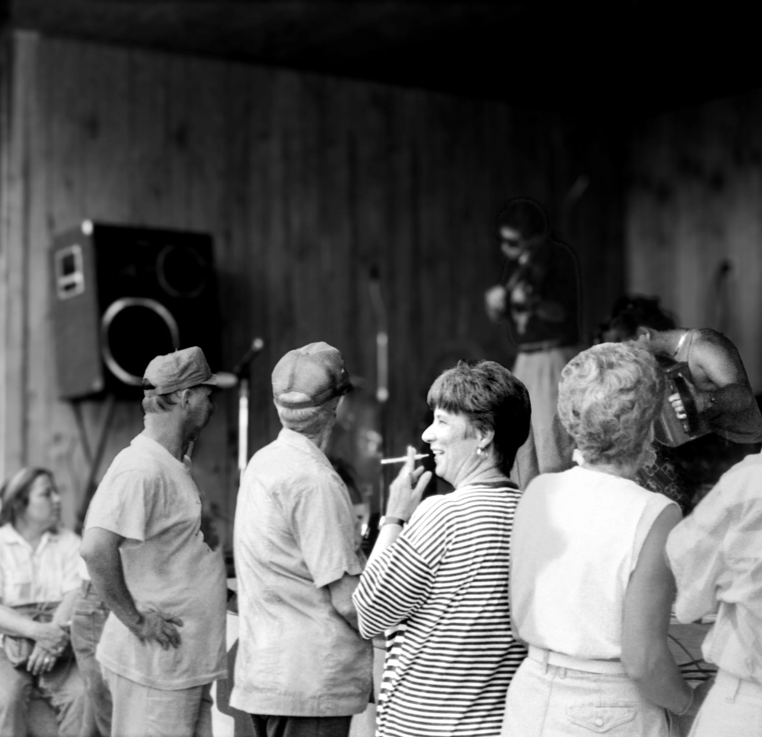 People socializing and smiling at a gathering with a speaker in the background.