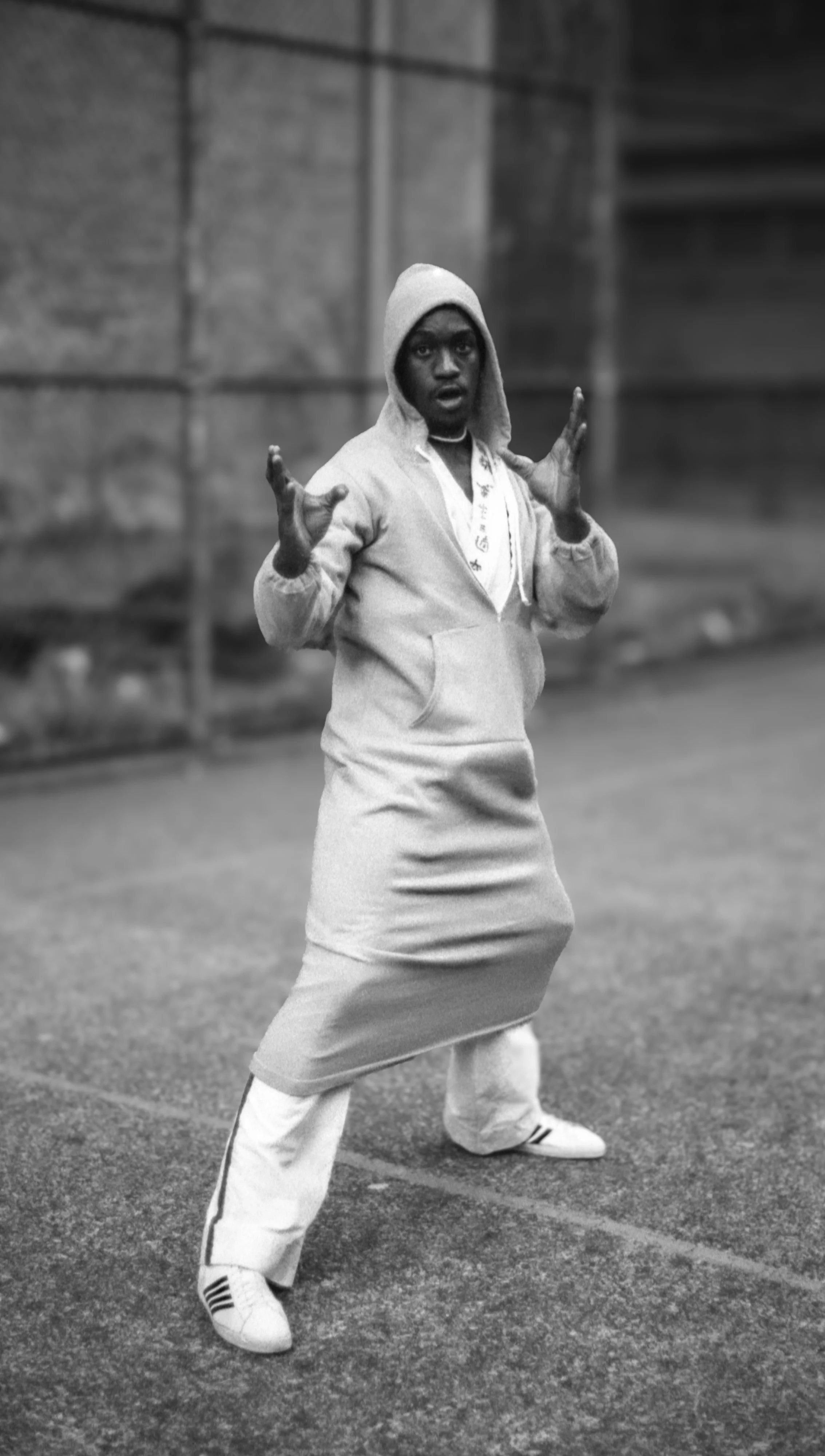 A woman wearing a hoodie, long skirt, and sneakers standing on a street with a surprised or expressive look.