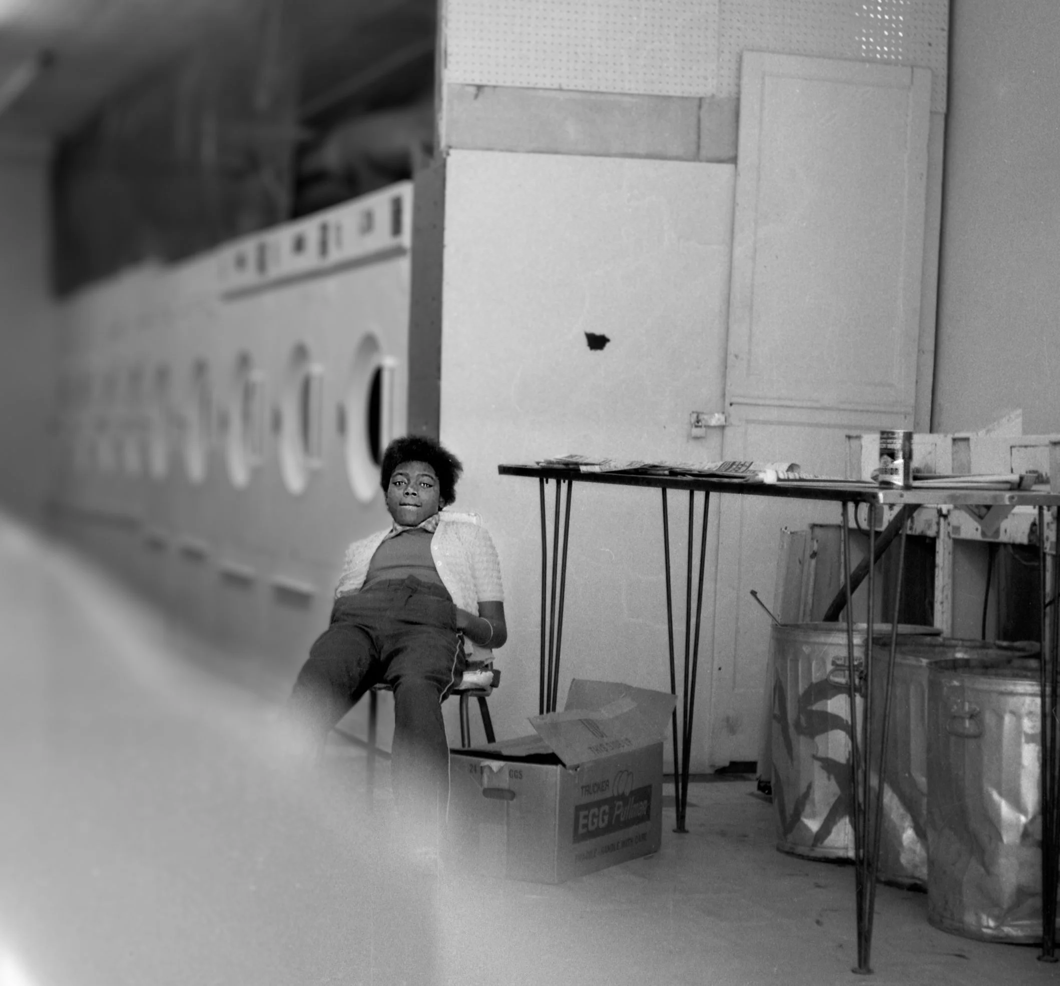 Young girl sitting on a chair in a laundry room with washing machines and laundry supplies around.