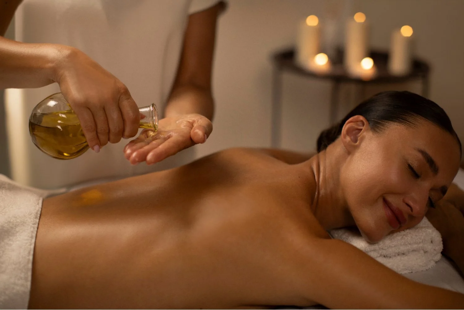 Una mujer recibe un masaje con aceites en la espalda en un ambiente de spa con velas encendidas en el fondo. Masaje tailandés con aceites. Aromaterapia.