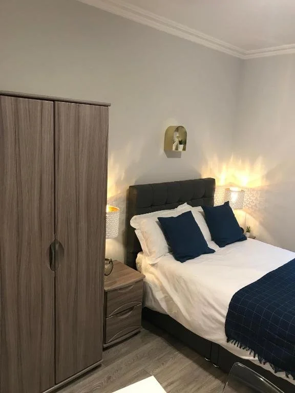 A bedroom with a bed, two bedside tables with lamps, a wardrobe, and a decorative shelf with plants on the wall.