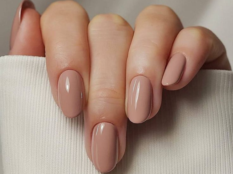 Close-up of a hand with neatly manicured oval-shaped nails painted in a glossy, nude color.