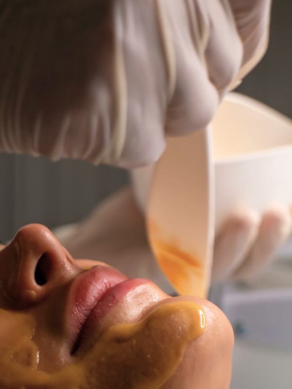 A person receiving a facial treatment with a facial mask being applied by a professional wearing gloves.