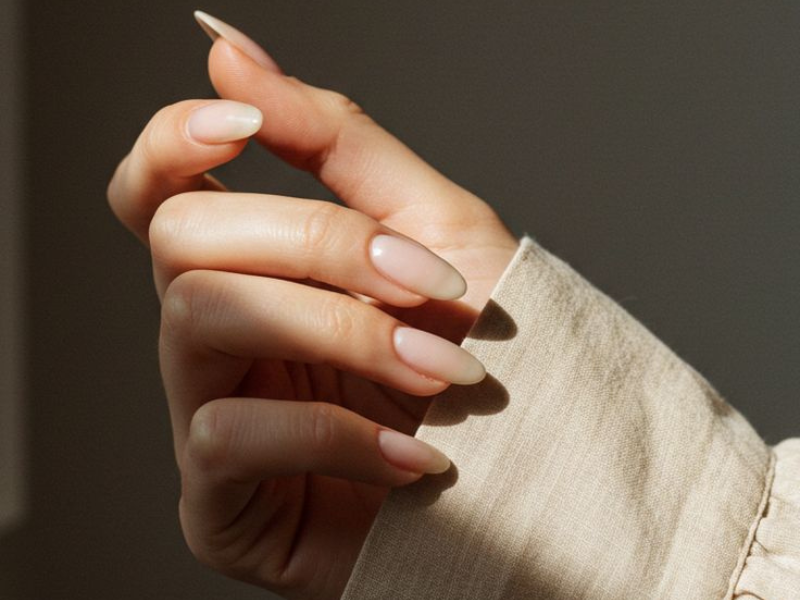 Close-up of a person's hand with long, well-manicured nails holding a piece of beige fabric.