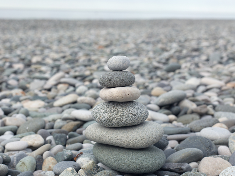 Stacked smooth stones on a pebbled beach with blurred shoreline in the background.