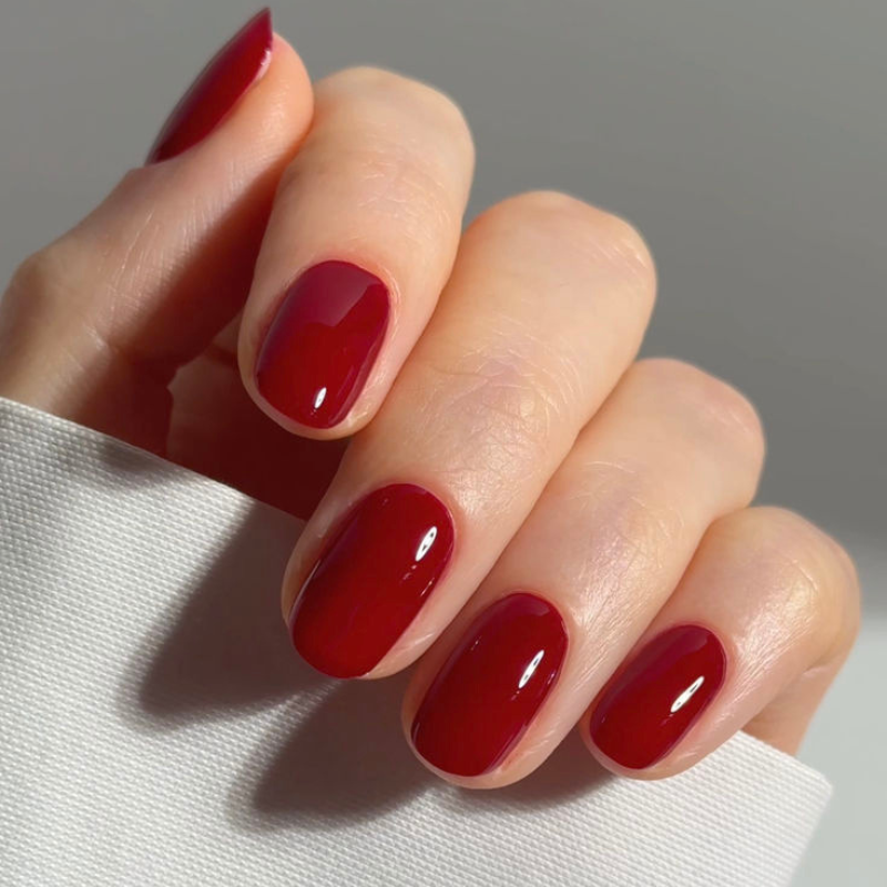 Close-up of a hand with neatly manicured nails painted in glossy red polish, holding a piece of white fabric.