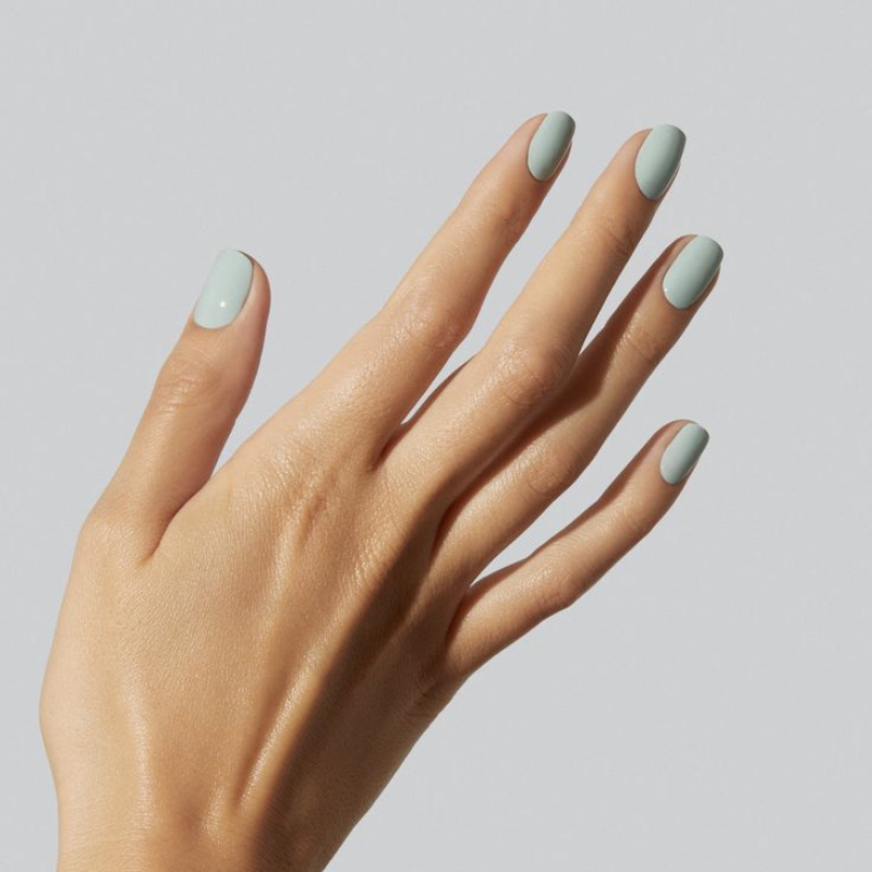 A hand with neatly manicured nails painted in light pastel blue against a plain light gray background.