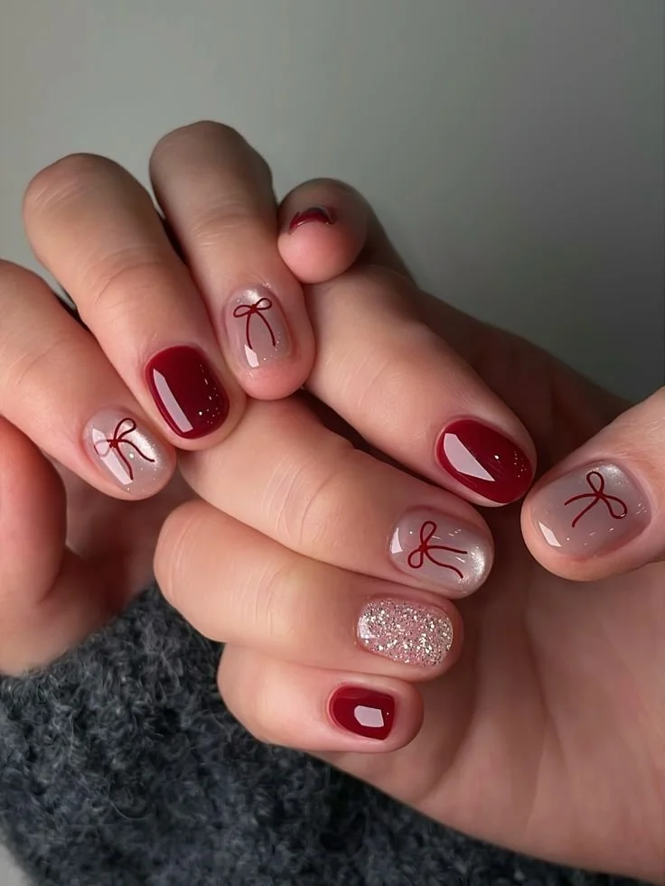 Manicured fingernails with red polish, gray polish with red bow design, and glitter polish on some nails.