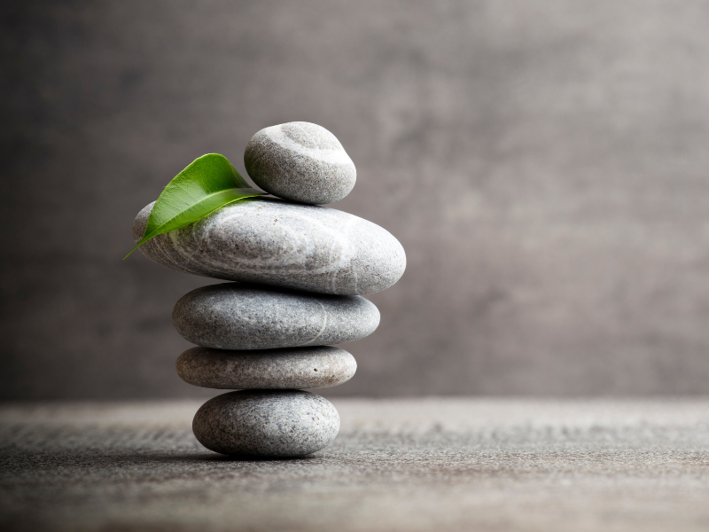 Stack of smooth gray stones with a green leaf on top, against a neutral background.