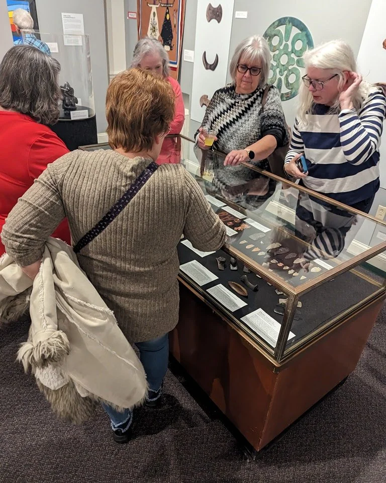 A group of women examining artifacts in a display case at a museum.