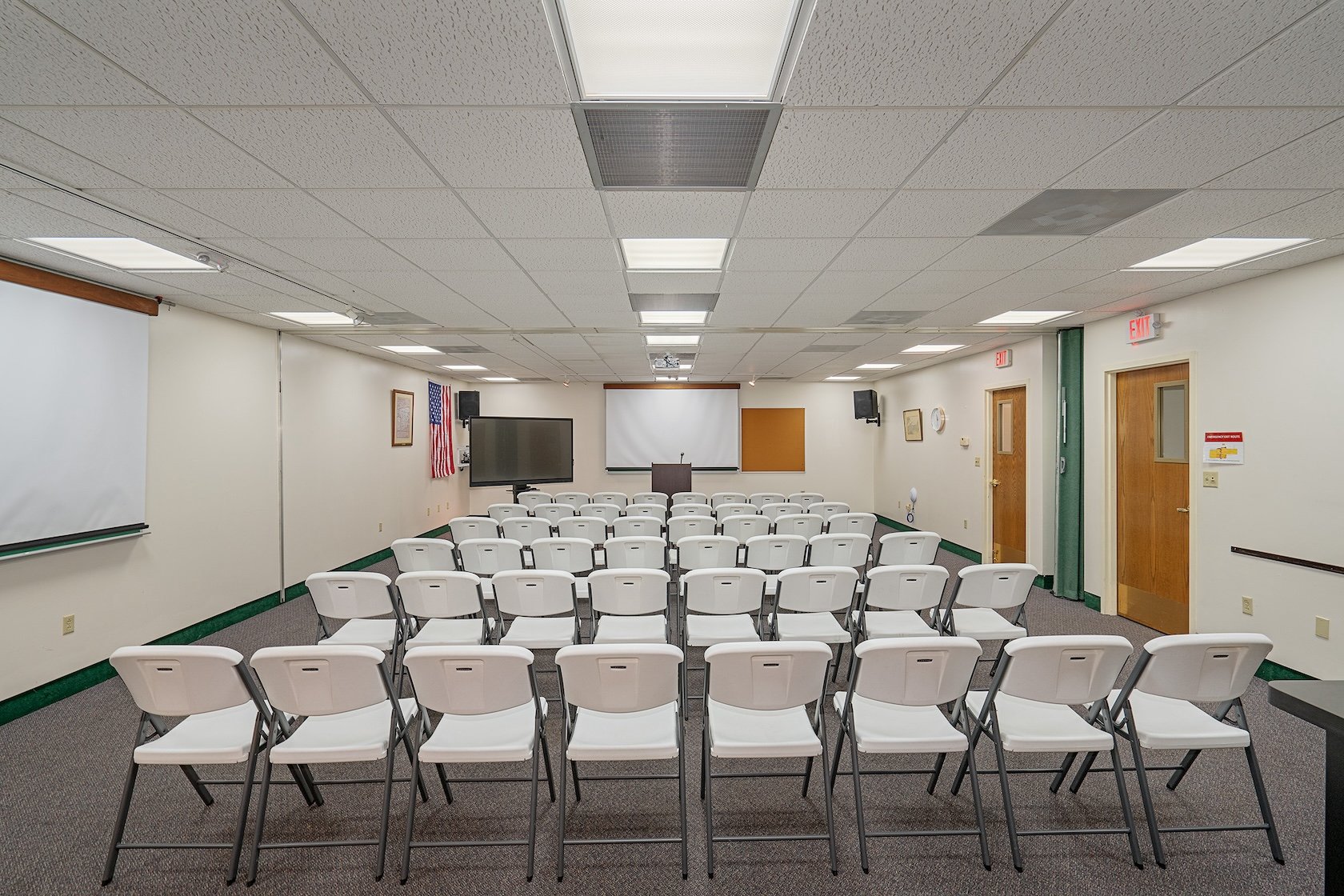 Empty classroom or meeting room arranged with white chairs facing a whiteboard and large screen at the front.