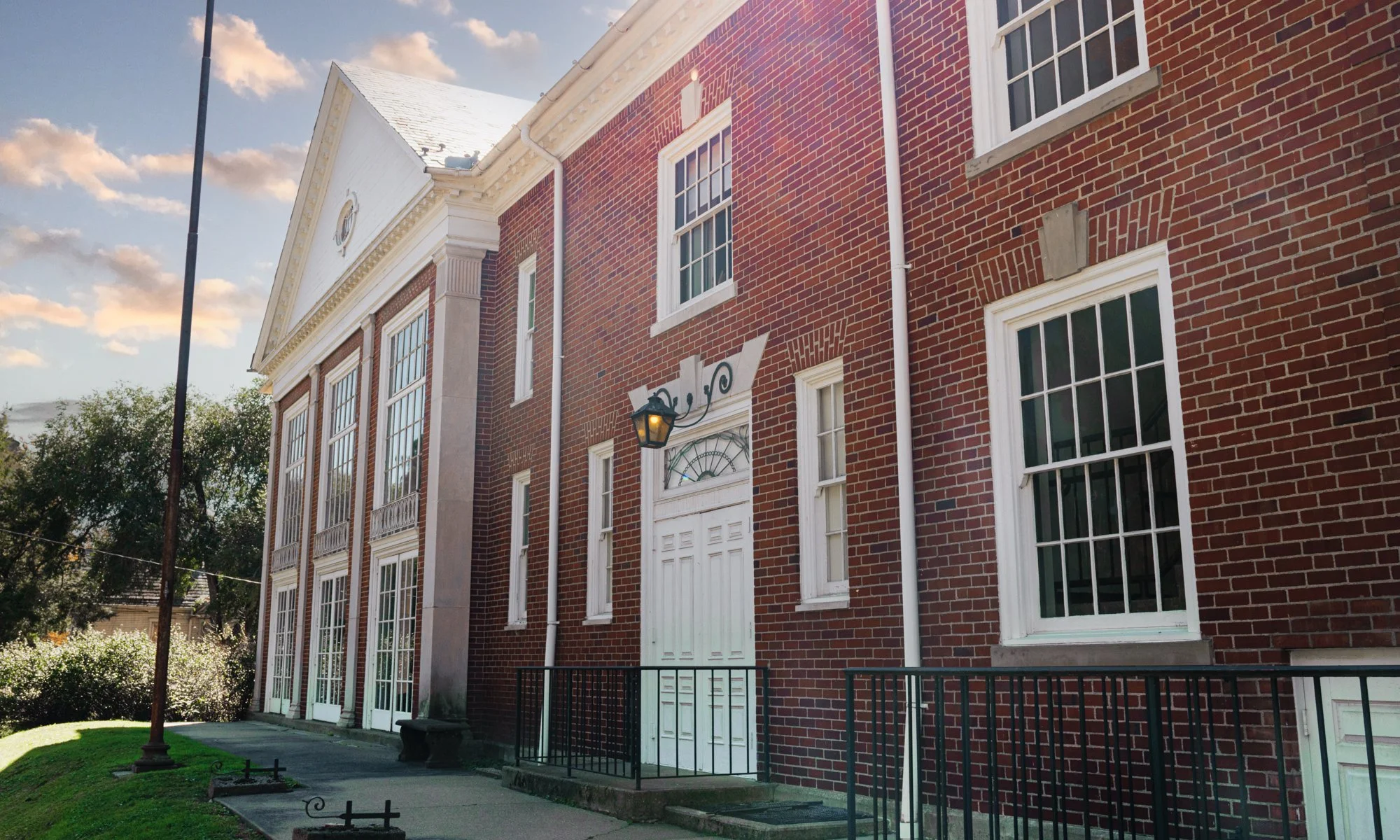 Historic red-brick building with white colonial-style trim, tall multi-pane windows, ornate entrance, and a lamppost.