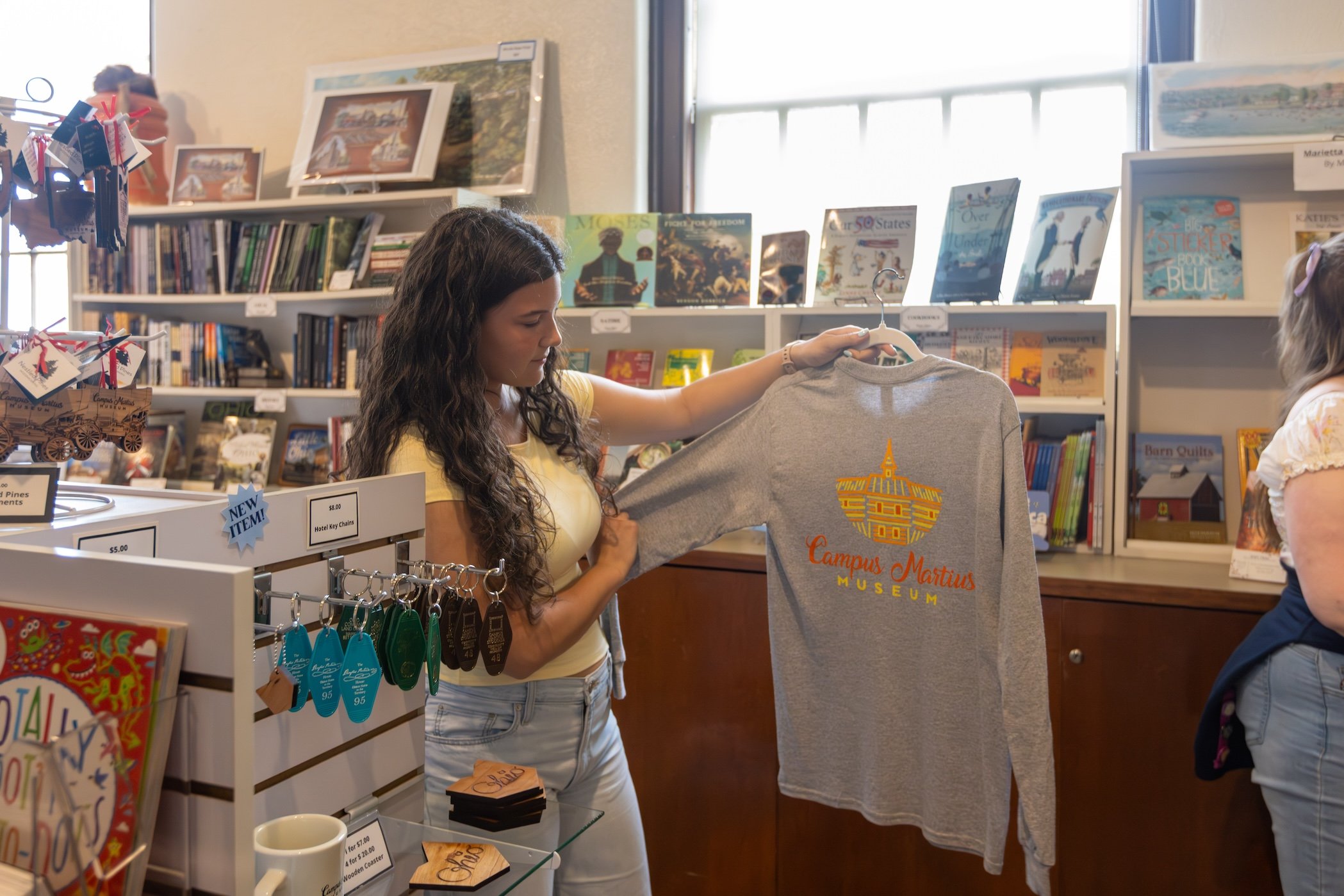 A woman shopping at a bookstore or gift shop, holding a gray sweatshirt with
