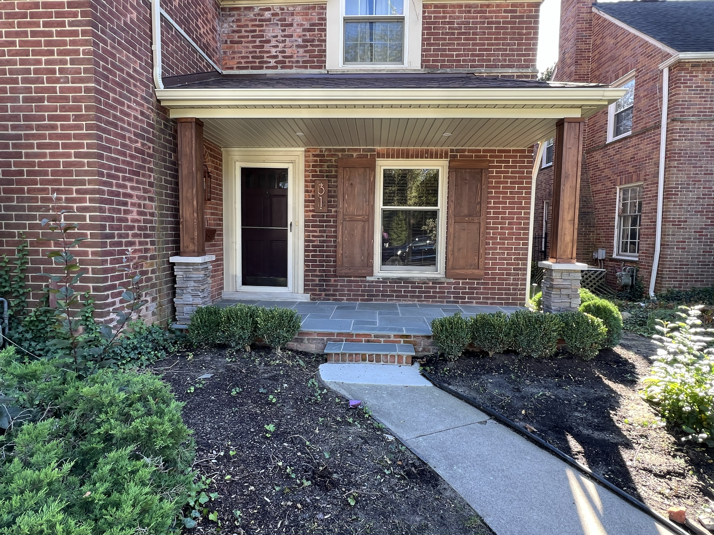 AFTER - Newly-constructed covered porch with stone-based cedar pillars, bluestone paver deck, lighting and custom-made cedar shutters