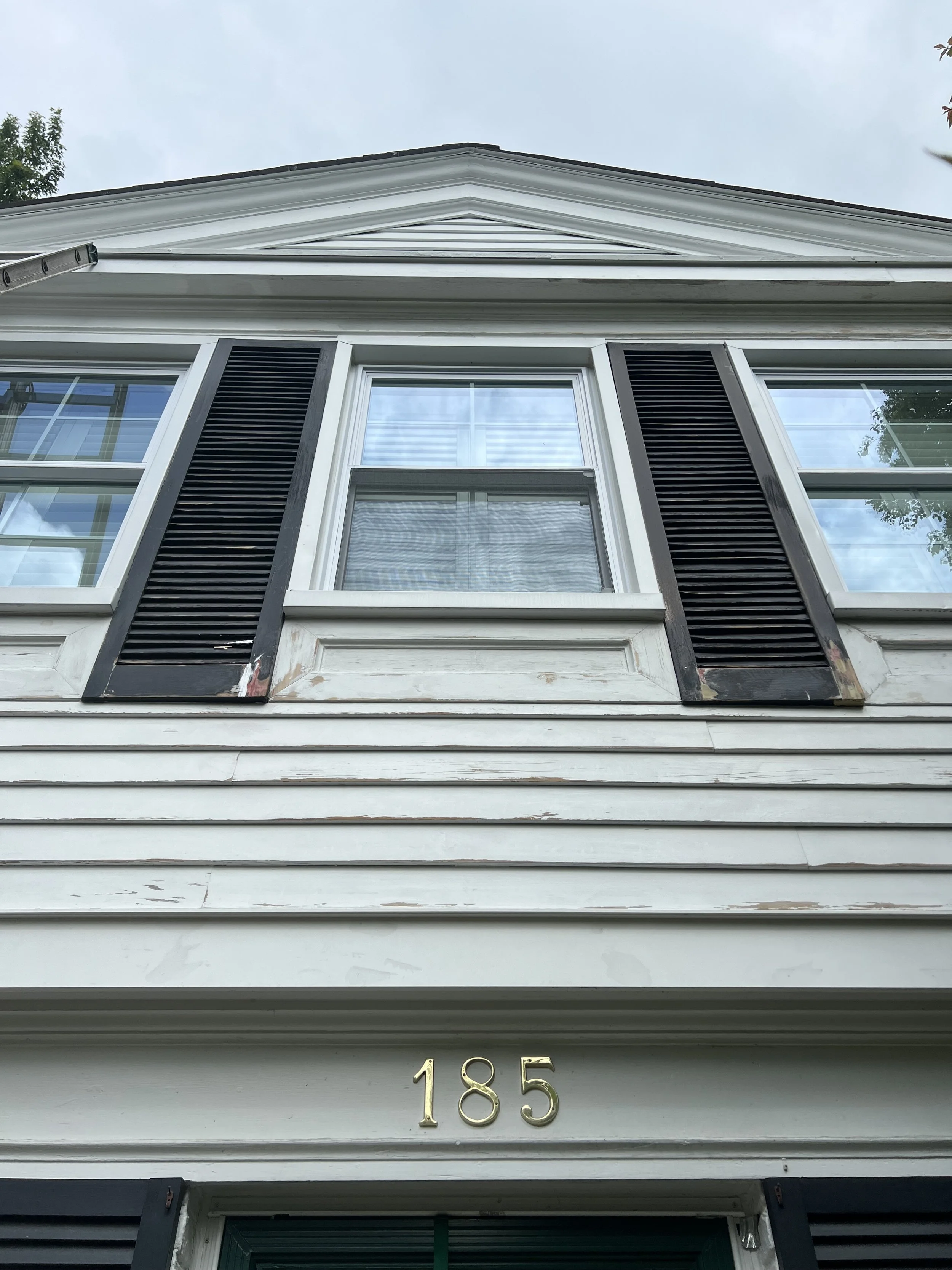 BEFORE - The wood clapboard siding, shutters and crown molding of this home were in bad shape. All of the elements had to sanded, filled and primed. In some areas, fully replacement was needed.