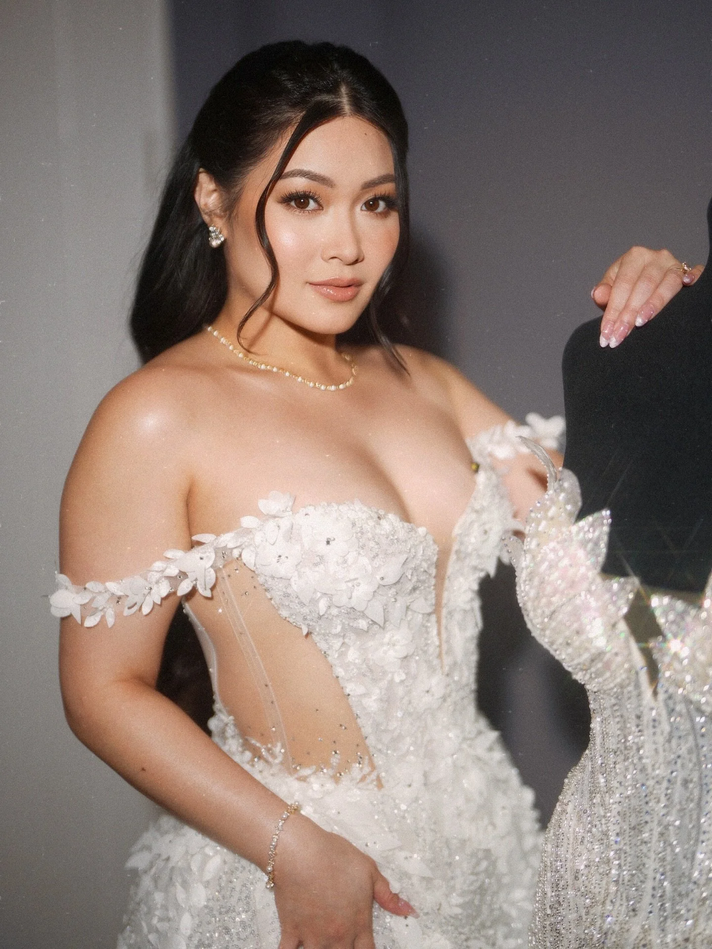 A woman wearing a white bridal gown with floral embellishments and a sweetheart neckline, posing for a photo.