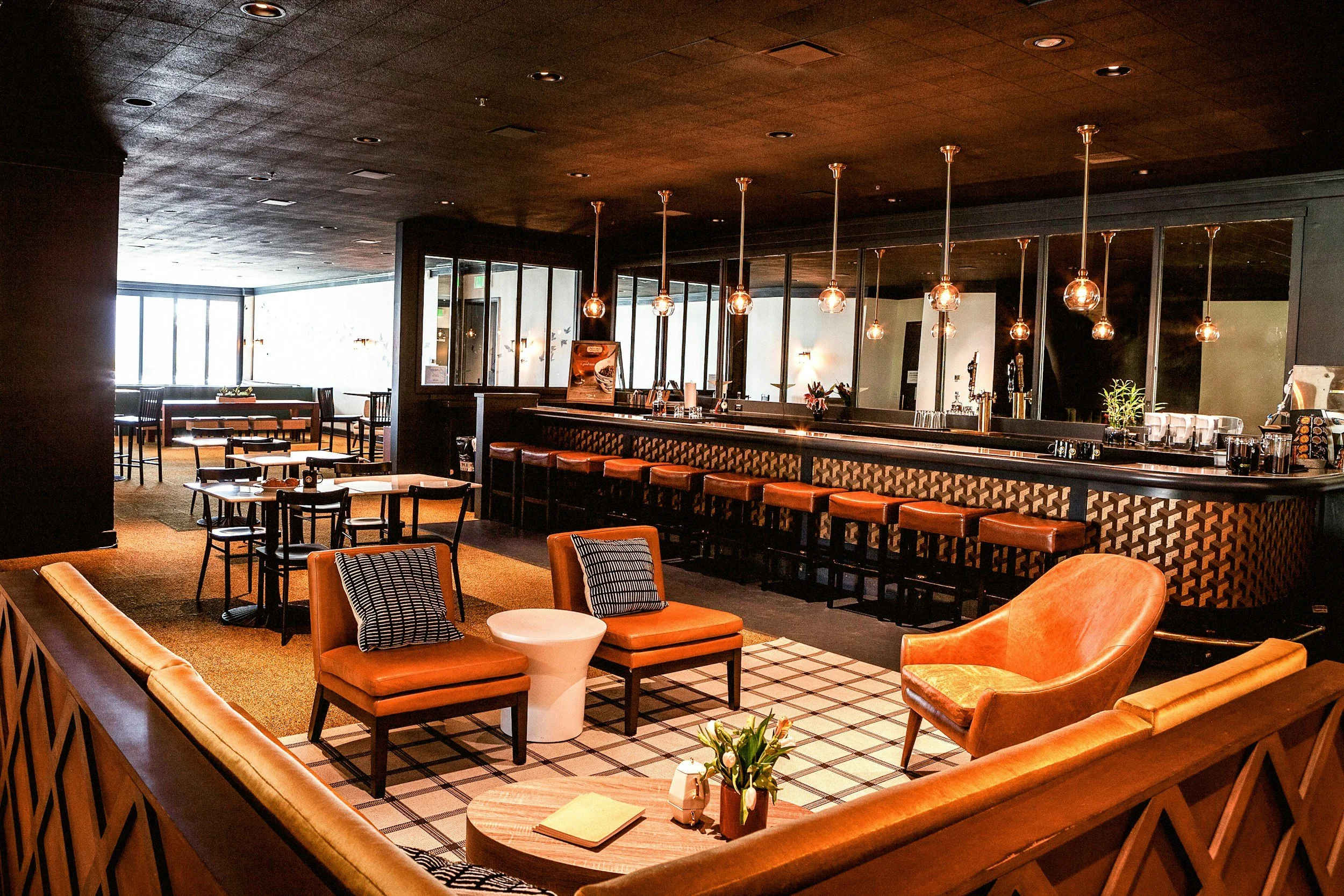 Interior of a modern bar and lounge with seating, including chairs and a bar counter with barstools, warm lighting, and a cozy, inviting atmosphere.