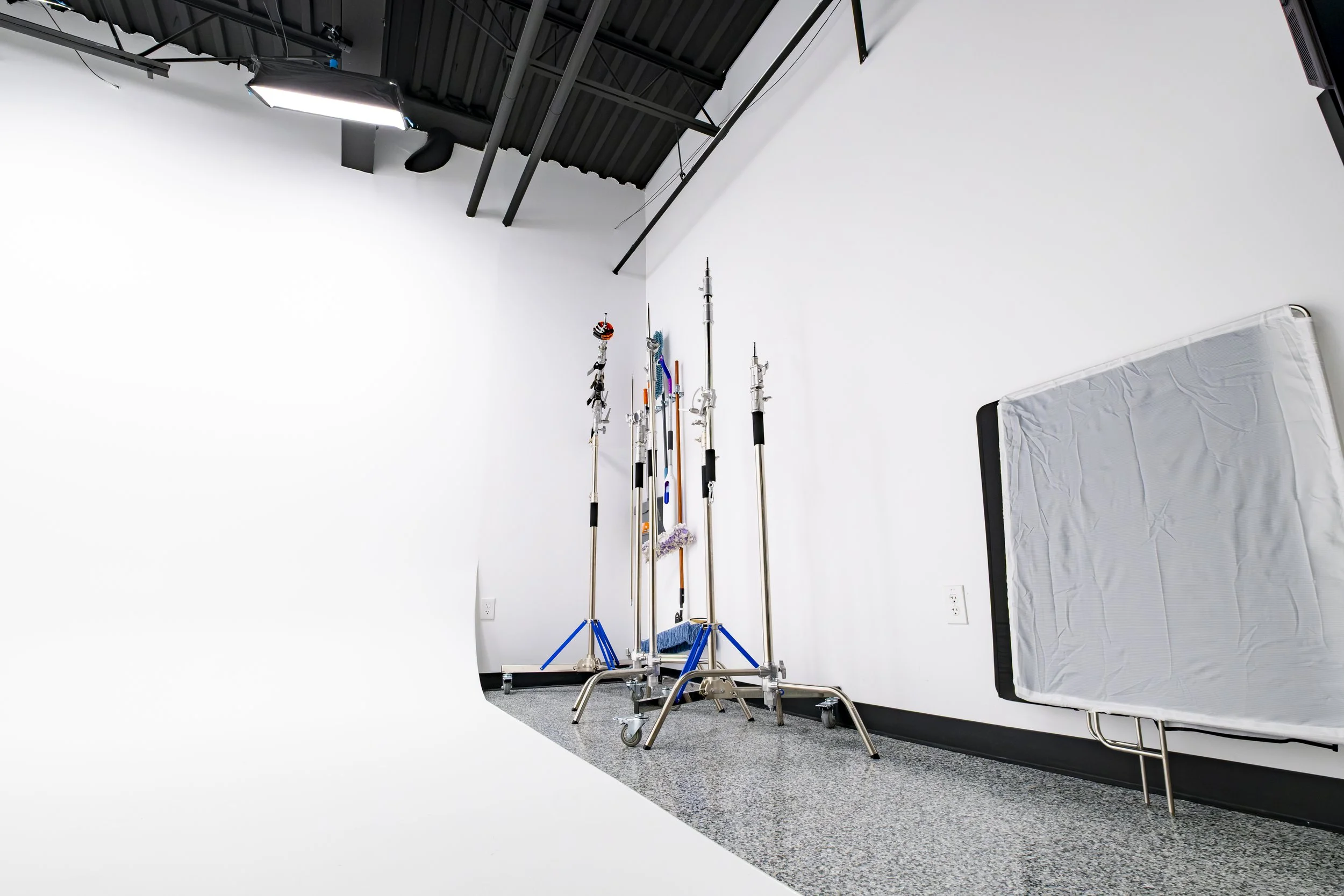 Photography studio with white cyclorama background, multiple lighting and camera equipment, and support poles for photography setup.