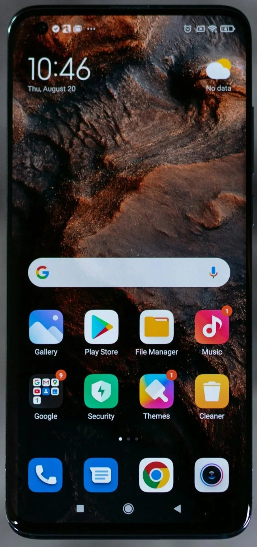 A smartphone displaying the home screen with app icons, time 10:46, date Thursday, August 20, and a background image of a rocky, textured surface.