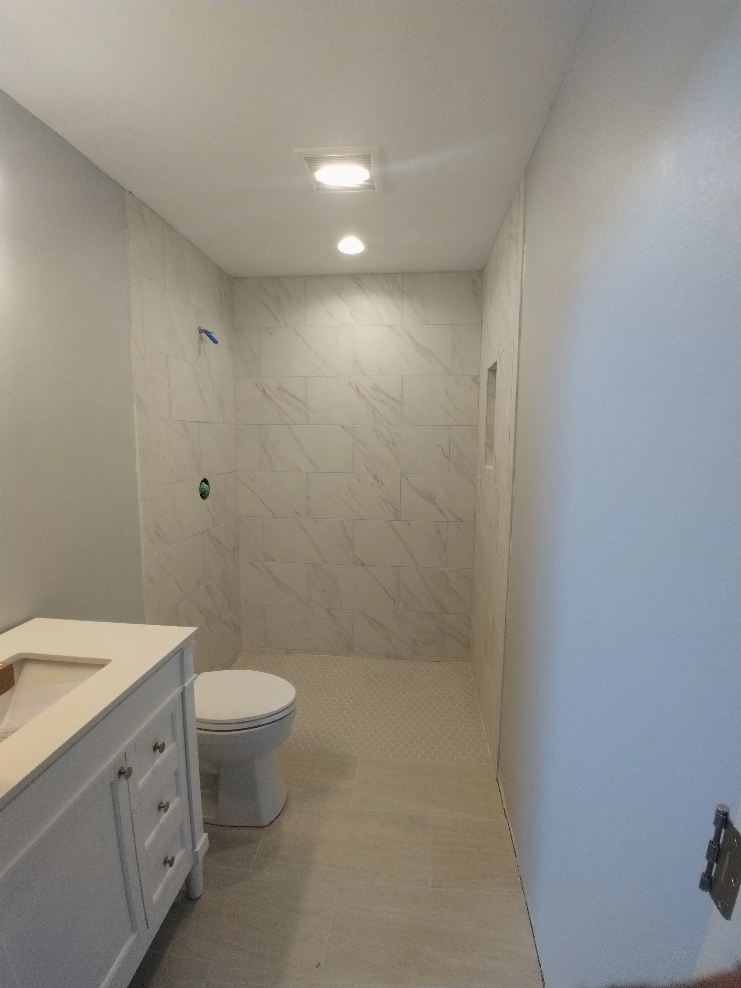 Bathroom under construction with unfinished shower area, white toilet, and vanity with sink, light-colored walls, and ceiling lights.