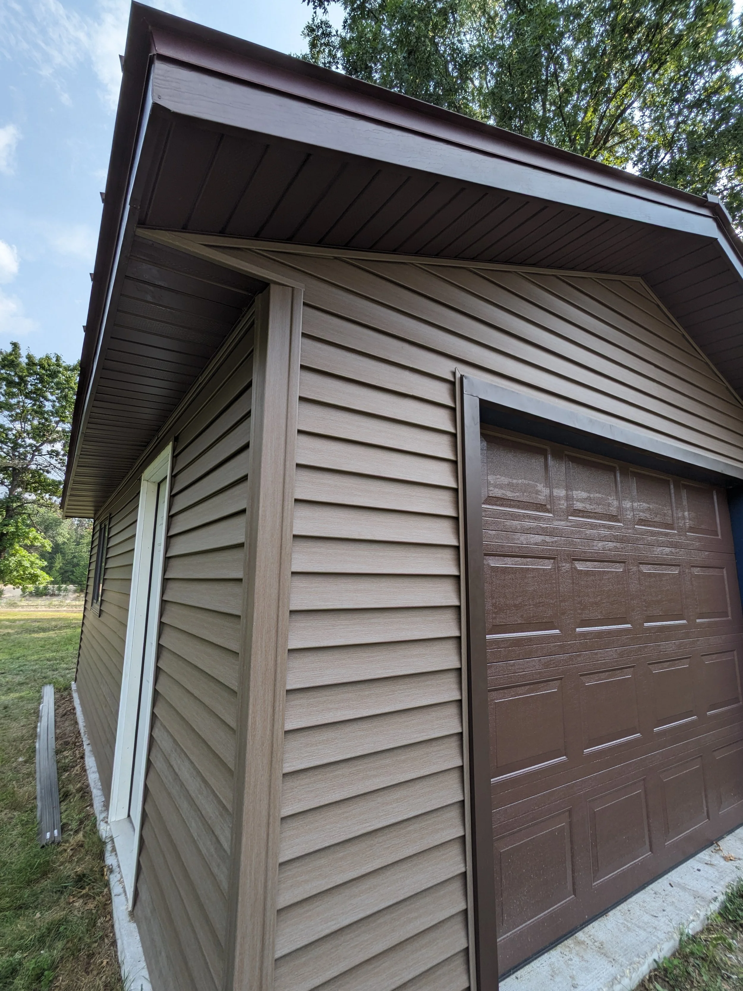 Close-up of a beige garage with tan vinyl siding and a brown garage door, shot from a low angle in daylight.